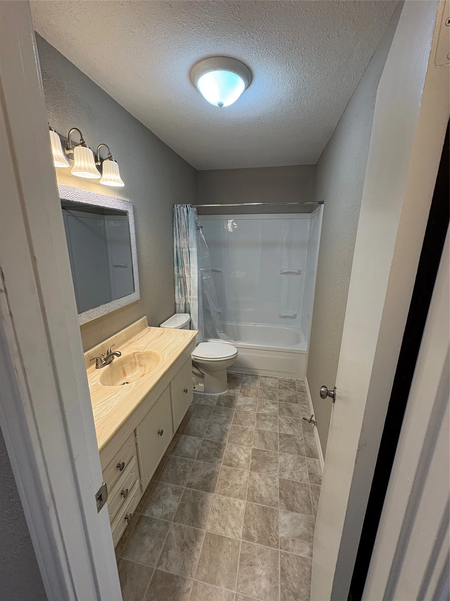 Bathroom featuring vanity, a textured ceiling, shower / bath combo with shower curtain, and stone finish floors.  Hall bath.