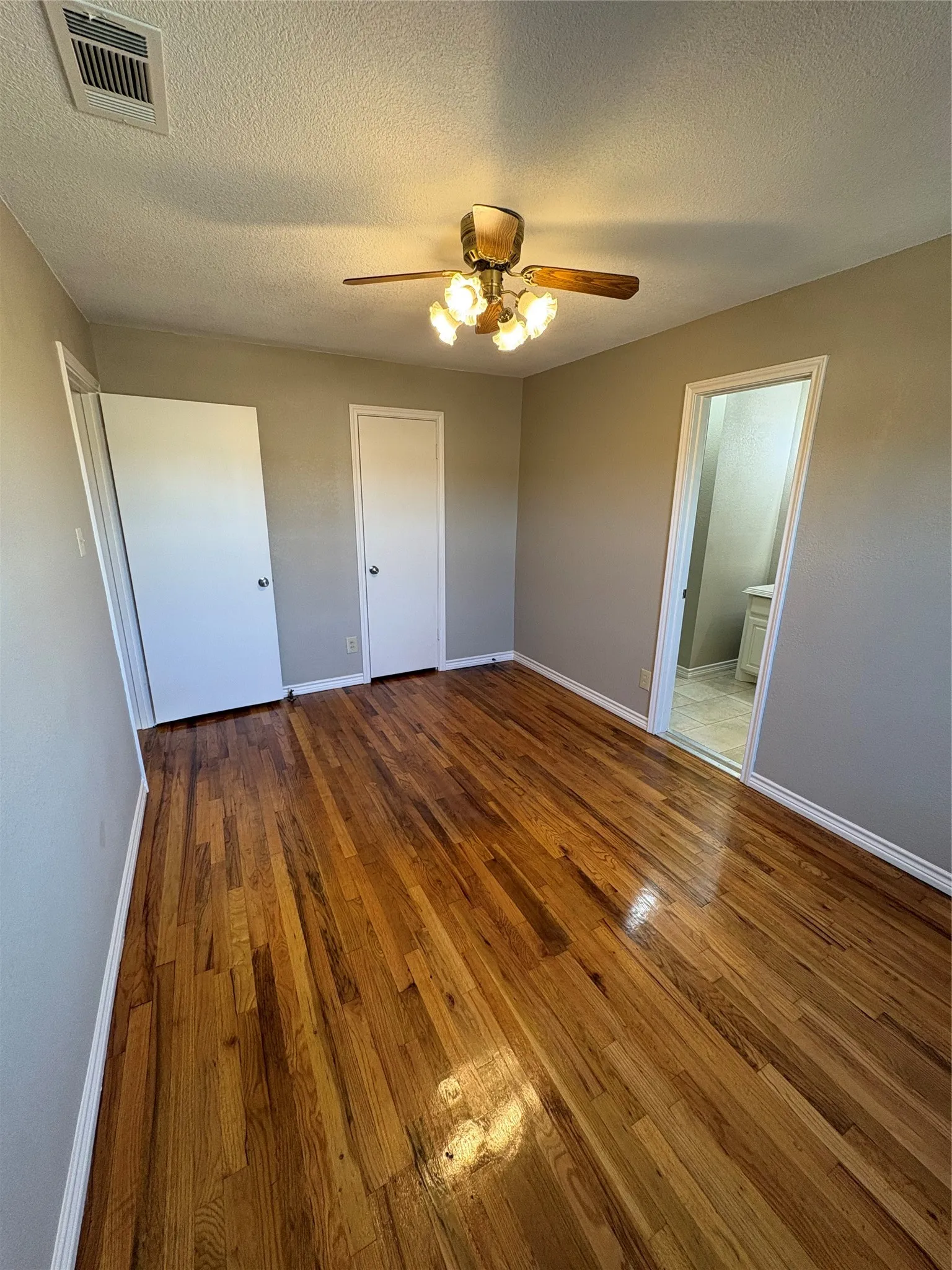 Unfurnished bedroom featuring dark wood-style flooring, a textured ceiling, and a ceiling fan