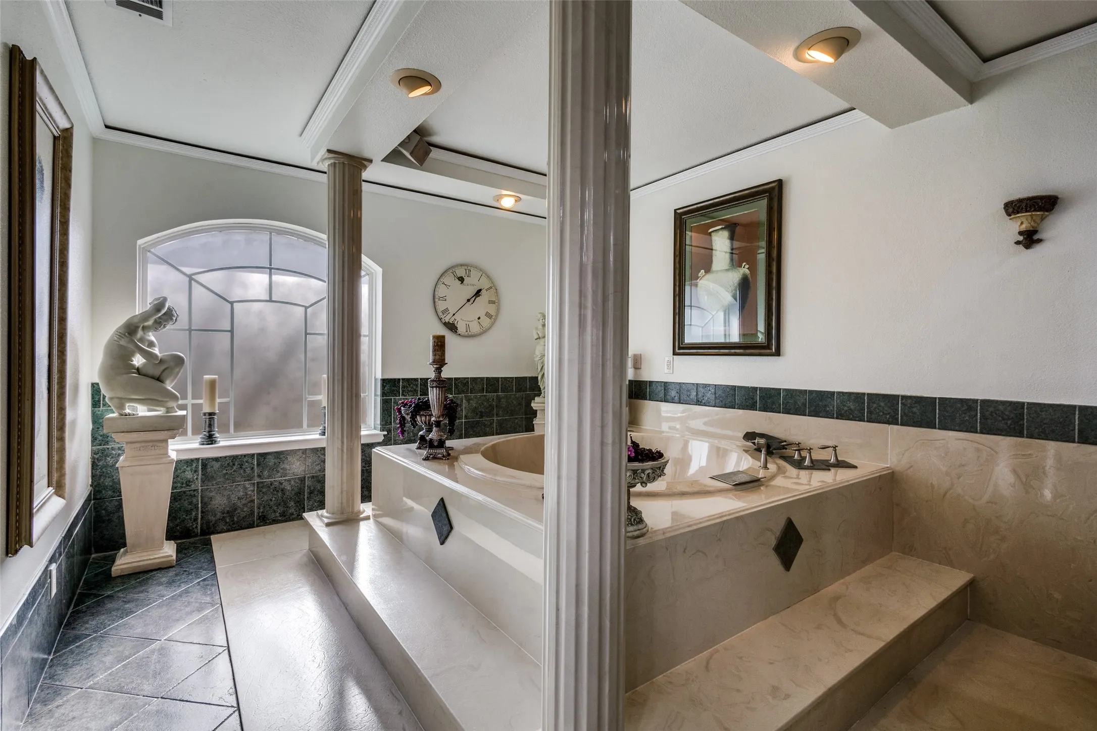 Marble platform jetted tub with column accents and arched privacy window. Tuscan-inspired details and elevated finishes create a distinctive primary bath setting.