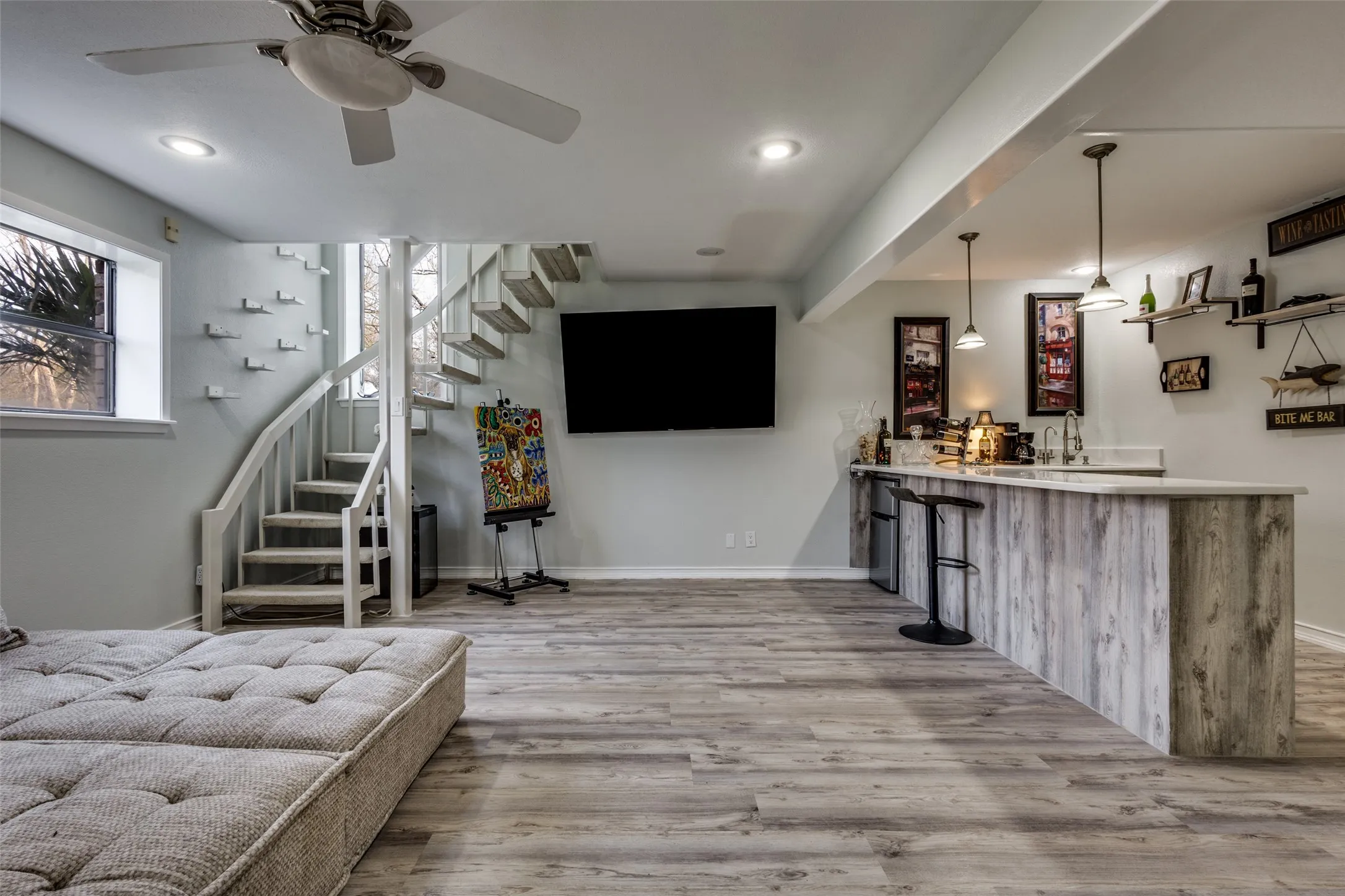Kitchenette/bar area on lower level with sink, under-counter refrigerator, storage cabinets, and pendant lighting. Ideal for media use, game nights, or guest suite flexibility.