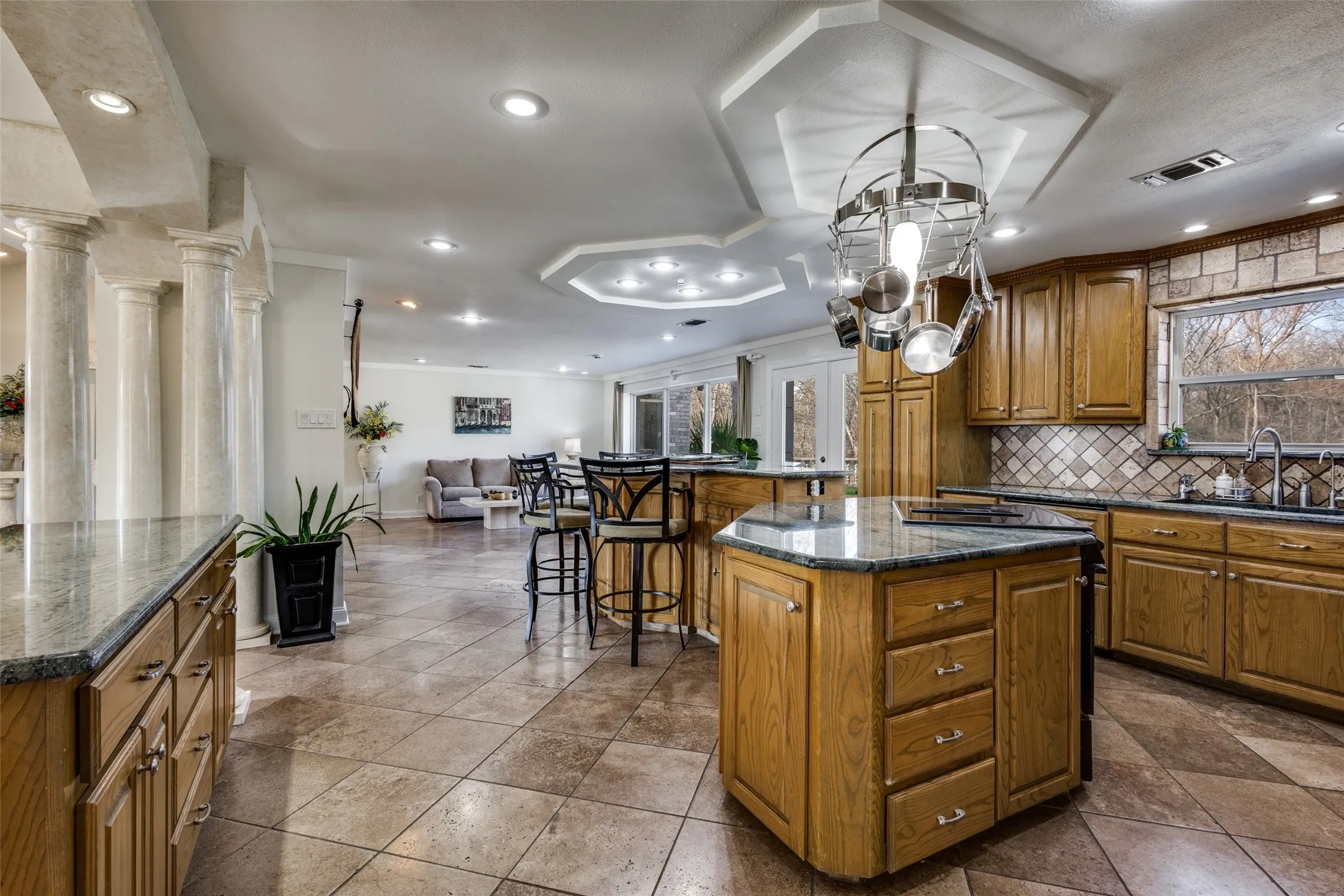 Open kitchen with granite counters, center island, and built-in wood-paneled refrigerator. Features electric oven and cooktop, tile backsplash, and ample cabinet storage. Overlooks adjacent living and dining areas for easy entertaining and everyday convenience.
