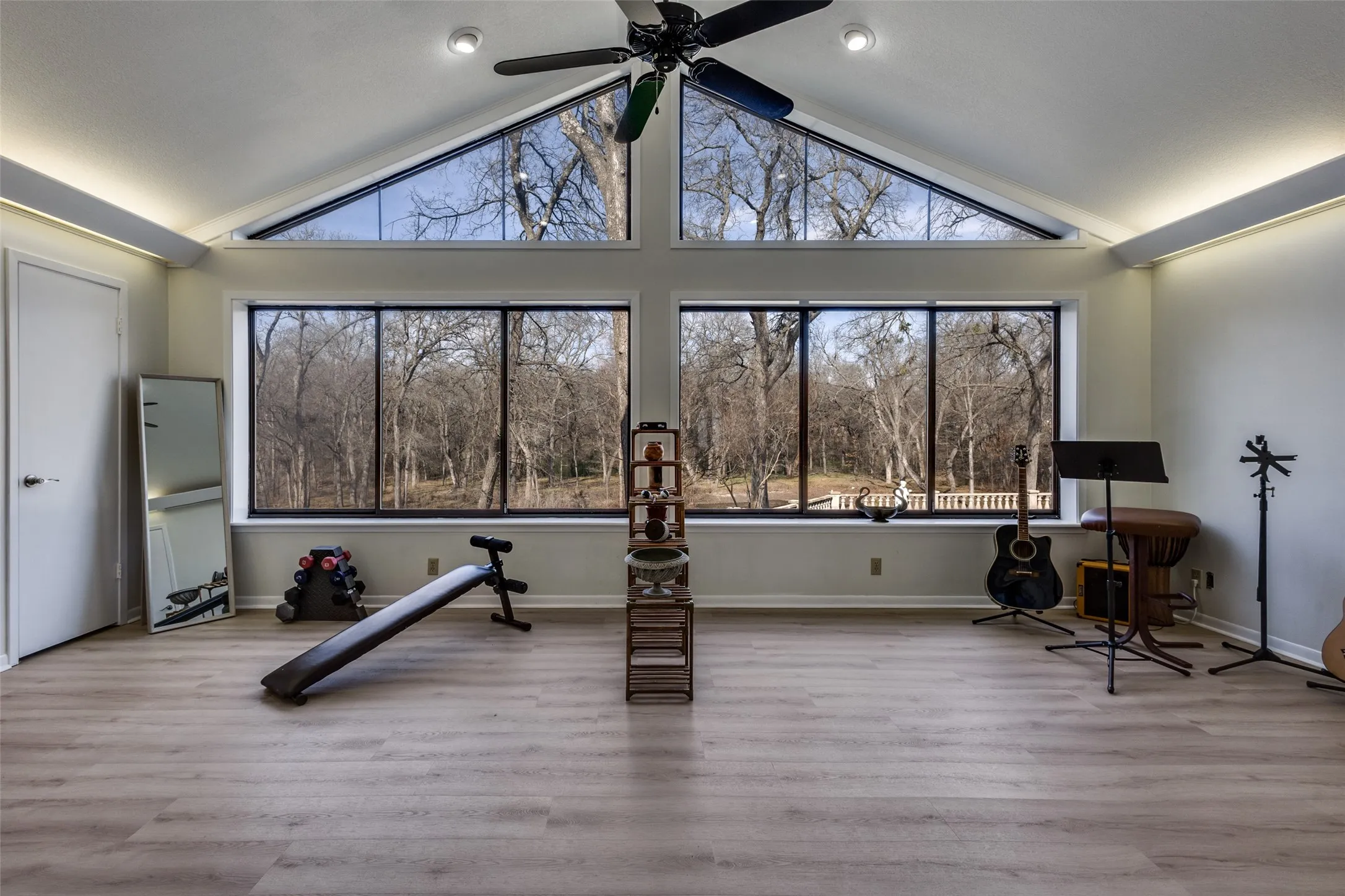 flex space off of the primary bedroom is ideal for workout equipment, studio use, or hobbies. French doors and large windows provide natural light and views of the wooded grounds. Additional access leads to the lower level for added convenience and separation of space.