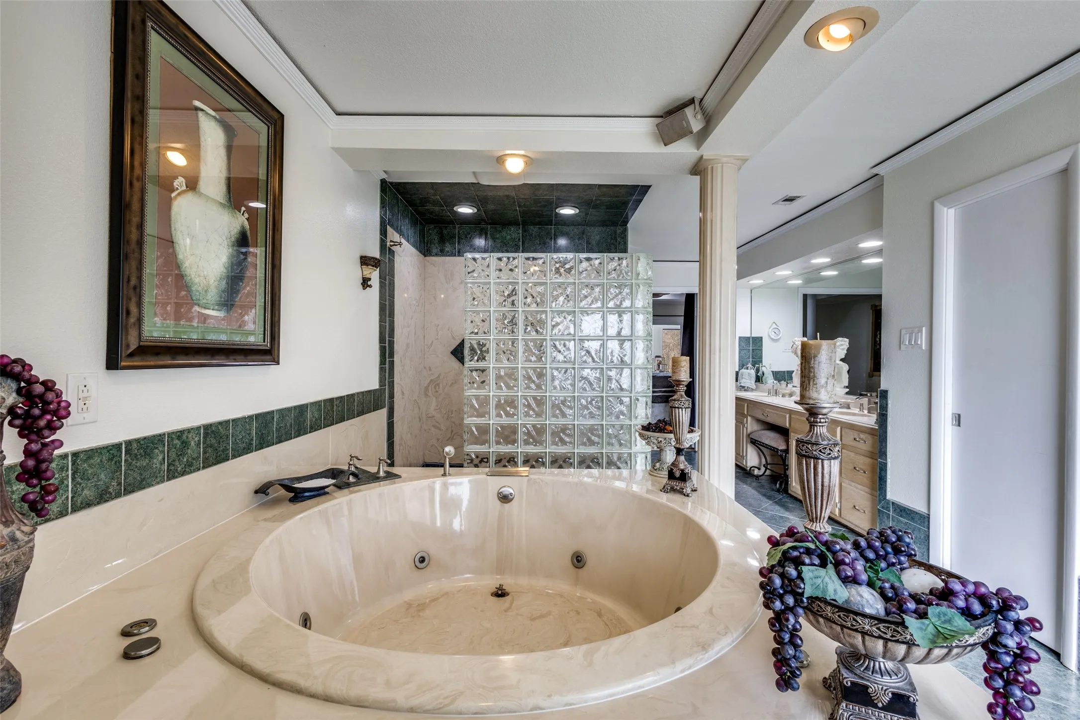 Glass block walk-in shower with adjacent jetted tub and extended vanity area. Ample lighting and classic architectural elements complete the primary bath layout.