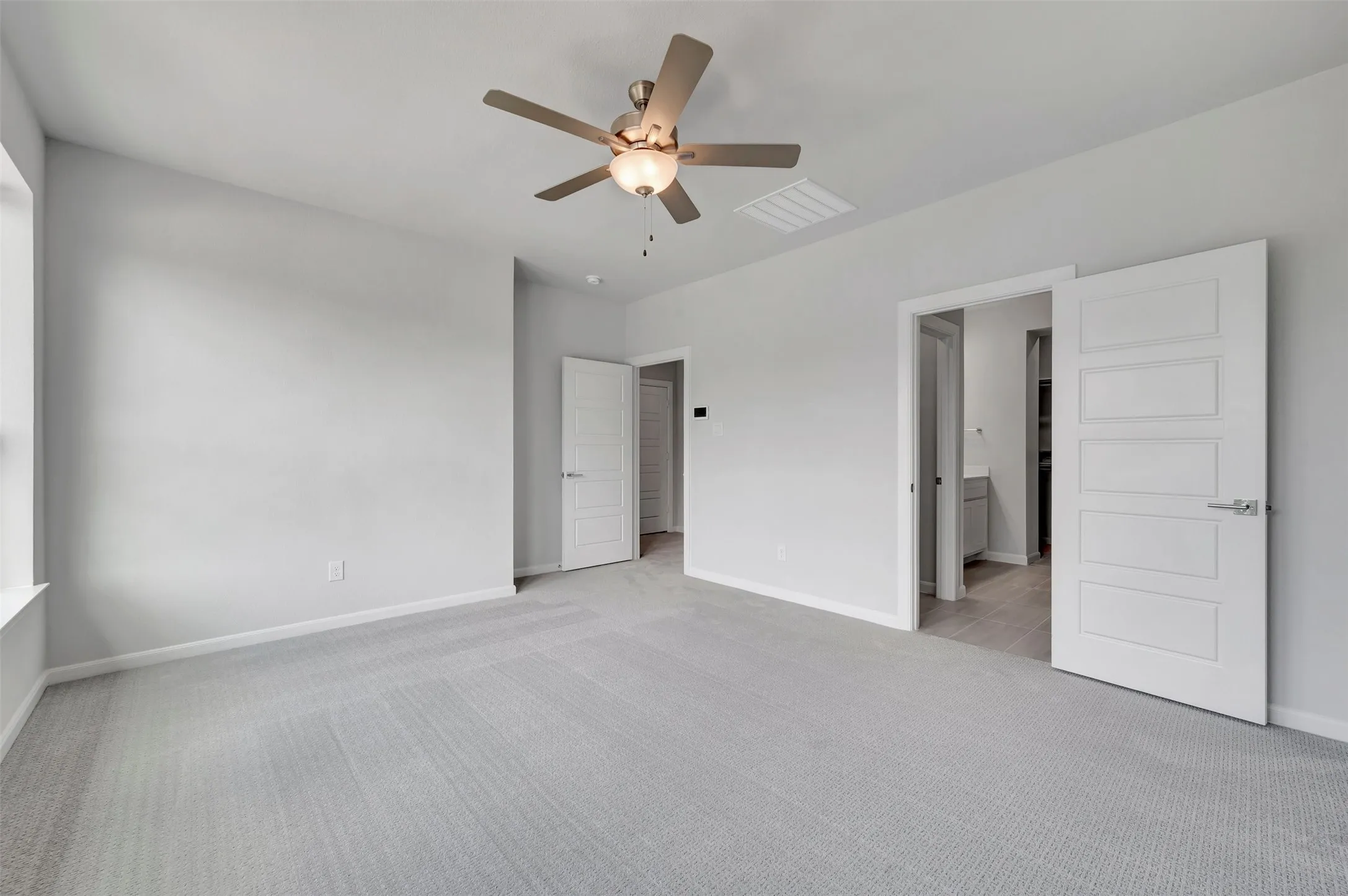 Spacious room featuring light gray carpeting, neutral wall finishes, and a contemporary ceiling fan with integrated lighting