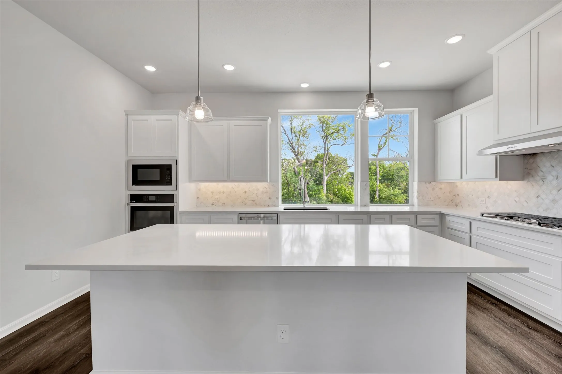 Kitchen featuring a spacious island with a white countertop, recessed lighting, pendant lights, wood-finish flooring, and white cabinetry