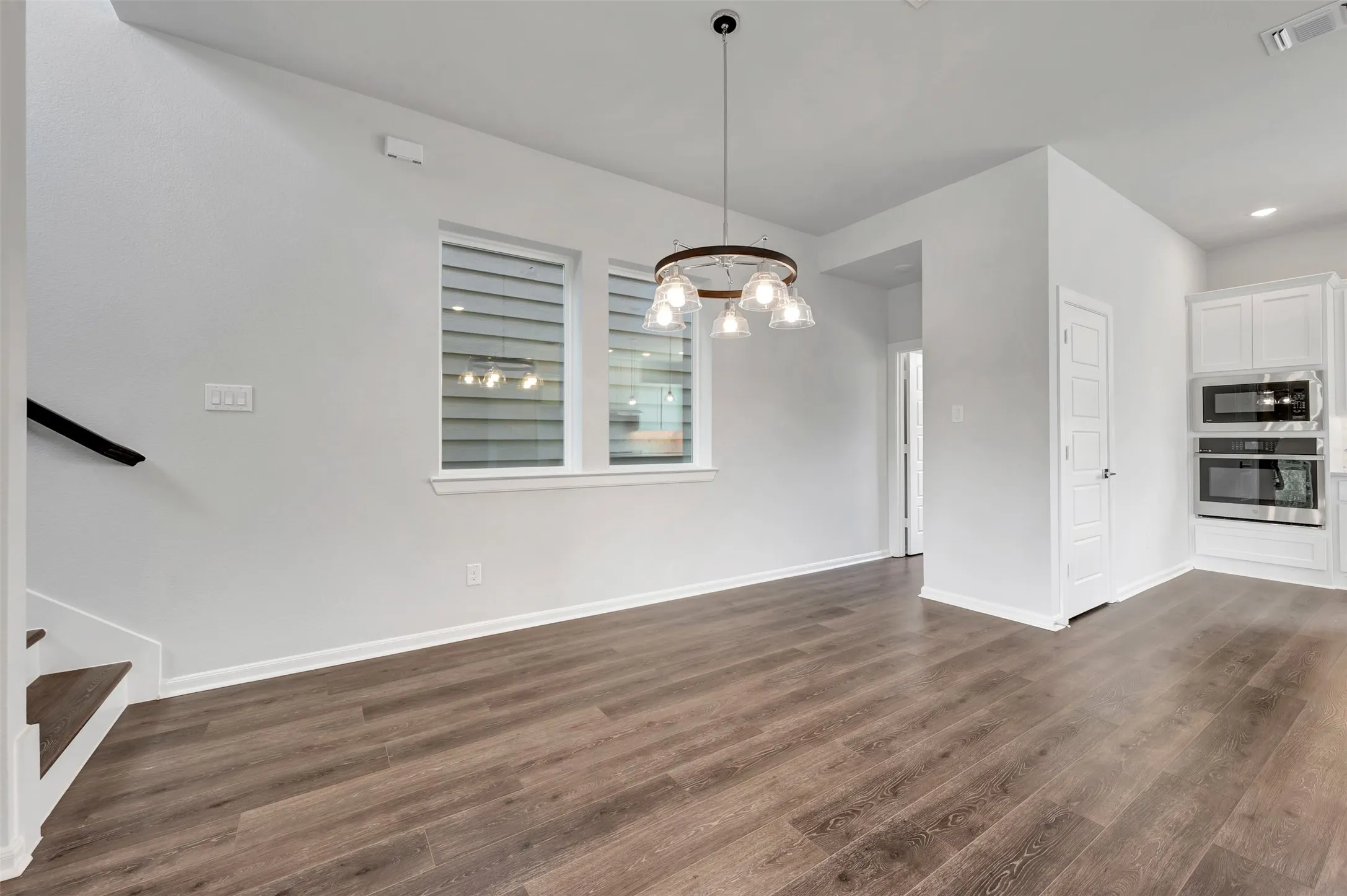 Spacious room featuring wood-finish flooring, white baseboards, and a contemporary chandelier