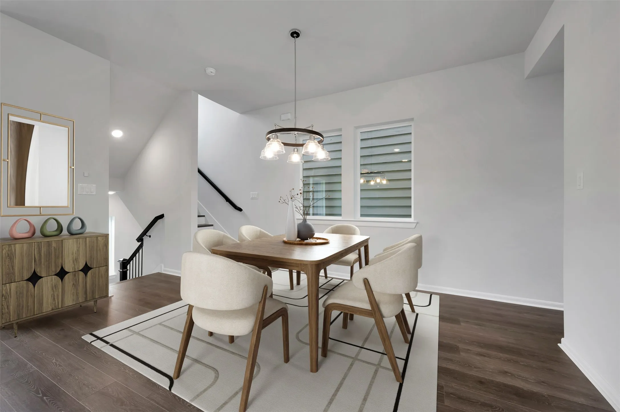 Open-concept dining area featuring wood-finish flooring, a contemporary chandelier, two windows with horizontal blinds, and access to a staircase with dark railings