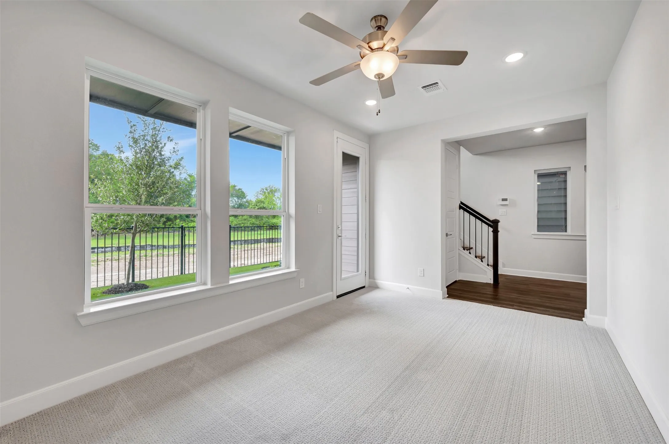 Carpeted living space featuring multiple windows, a ceiling fan with integrated lighting, recessed lighting, and a glass-paneled door
