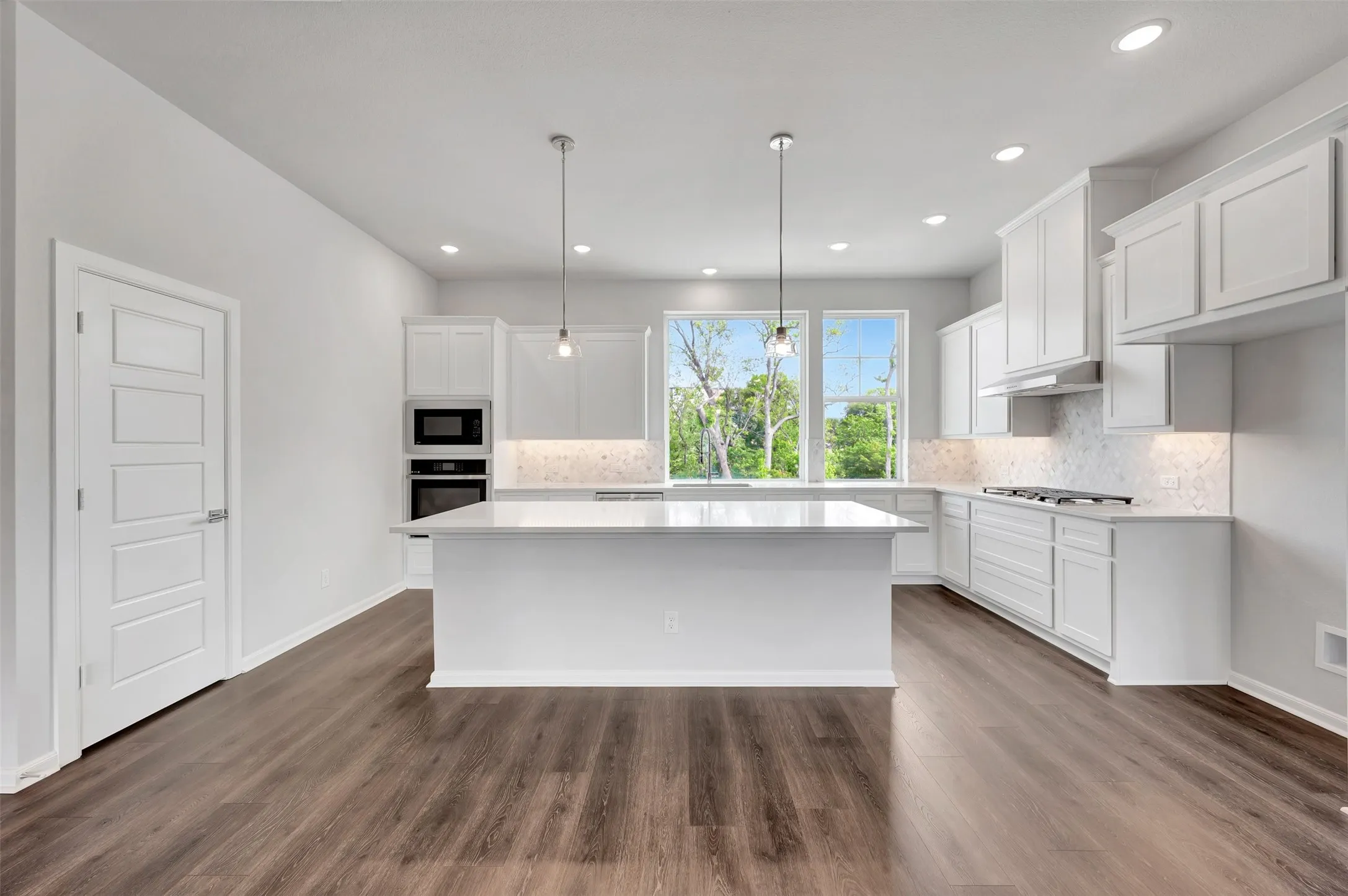 Kitchen featuring a central island with countertop seating, white shaker-style cabinetry, stainless steel appliances including a wall oven and microwave, a gas cooktop, and wood-finish flooring