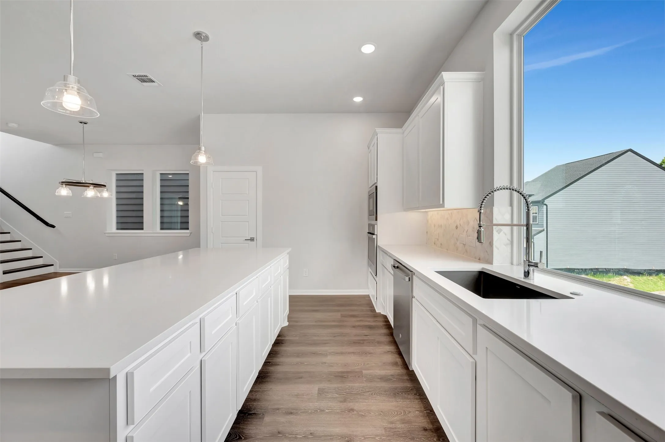 Modern kitchen featuring an expansive island with white cabinetry, wood-finish flooring, a large window, a stainless steel dishwasher, and a built-in oven