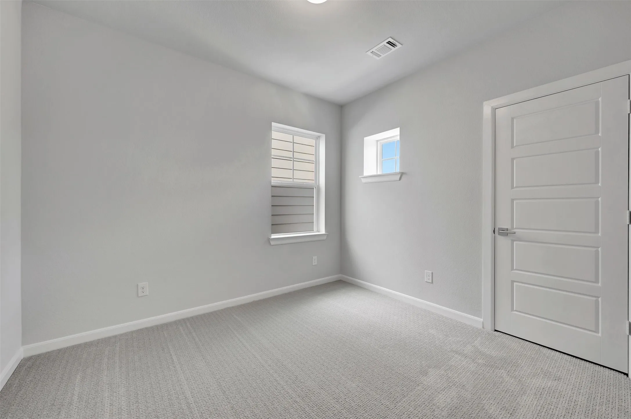 Light-filled room featuring carpet flooring, two windows, and a five-panel interior door
