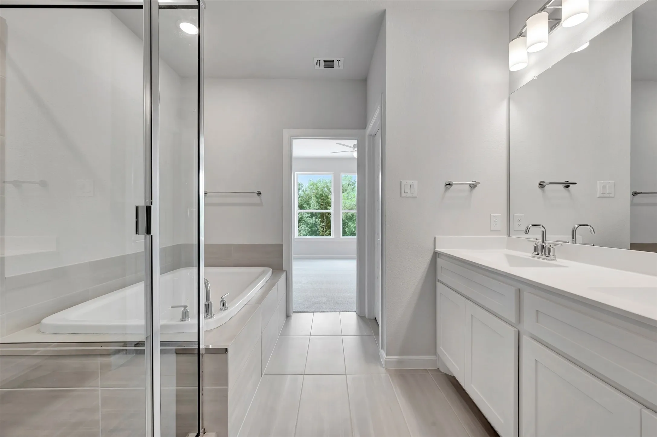 Bathroom featuring a dual vanity with white cabinetry and countertops, a large mirror with a three-light fixture, a built-in tub, and a separate glass-enclosed shower