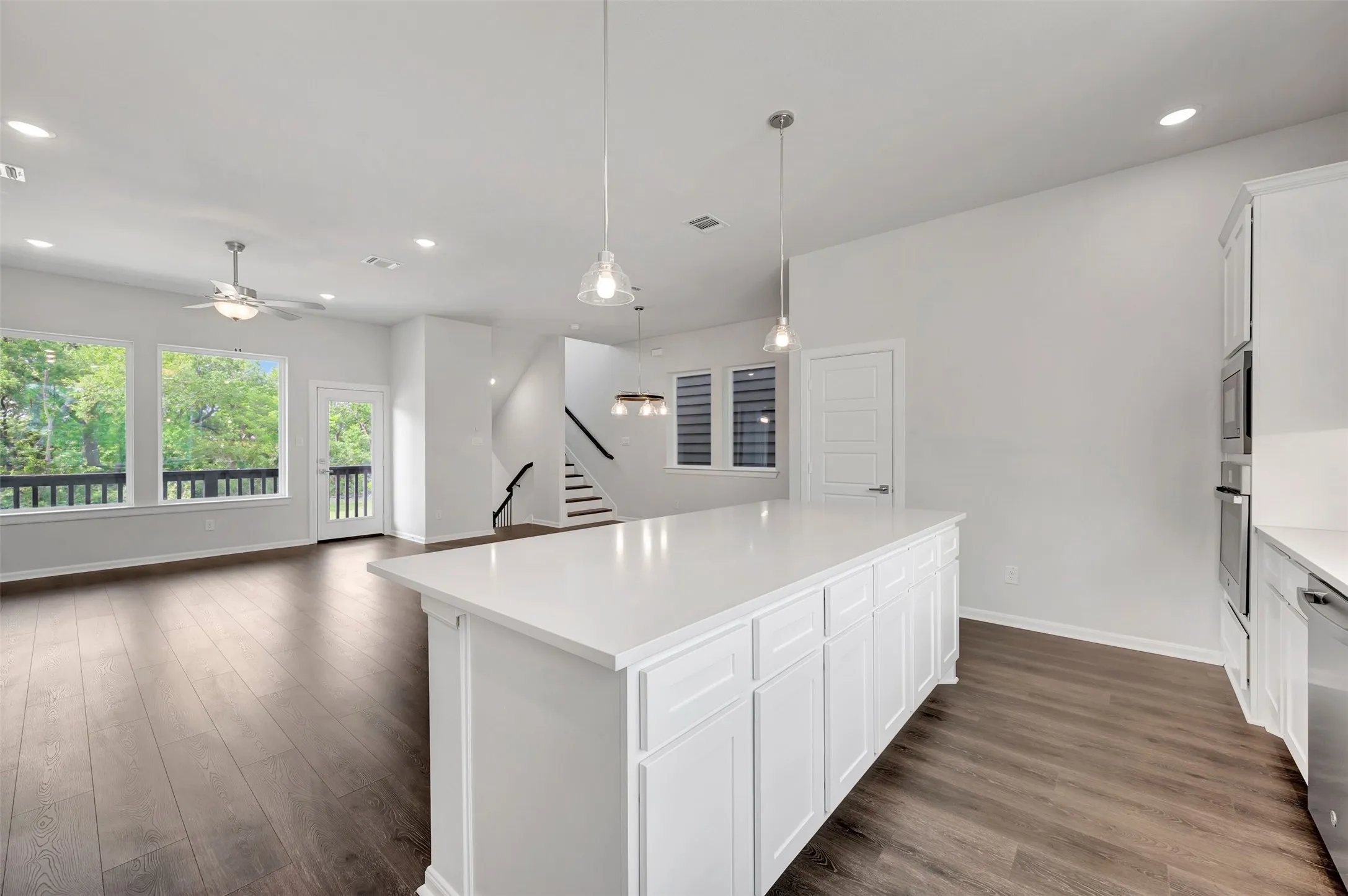 Spacious kitchen island with a light-toned countertop, white cabinetry, wood-finish flooring, recessed lighting, and a modern ceiling fan