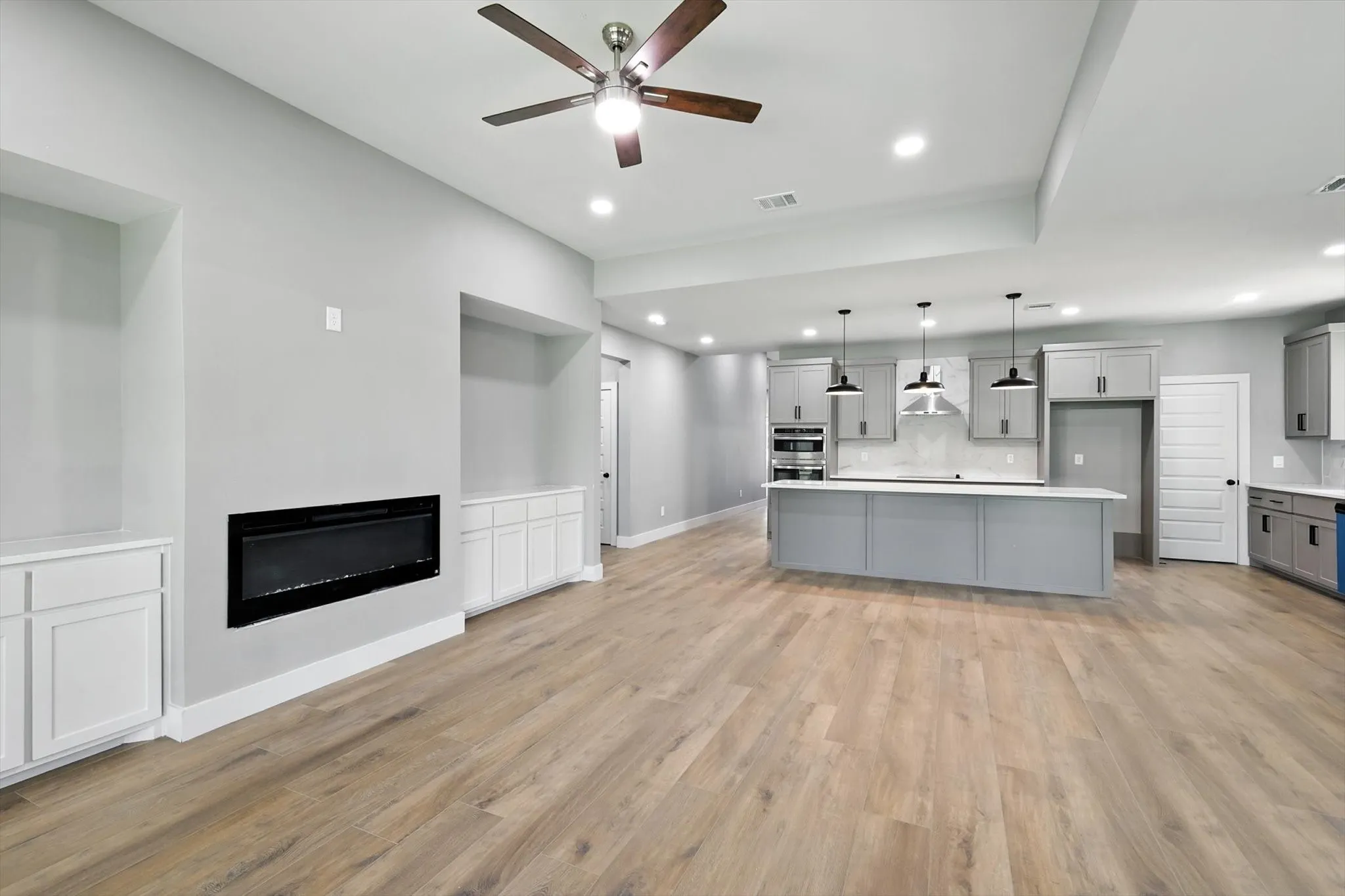 Kitchen with gray cabinetry, a kitchen island with sink, pendant lighting, light wood-style floors, and recessed lighting