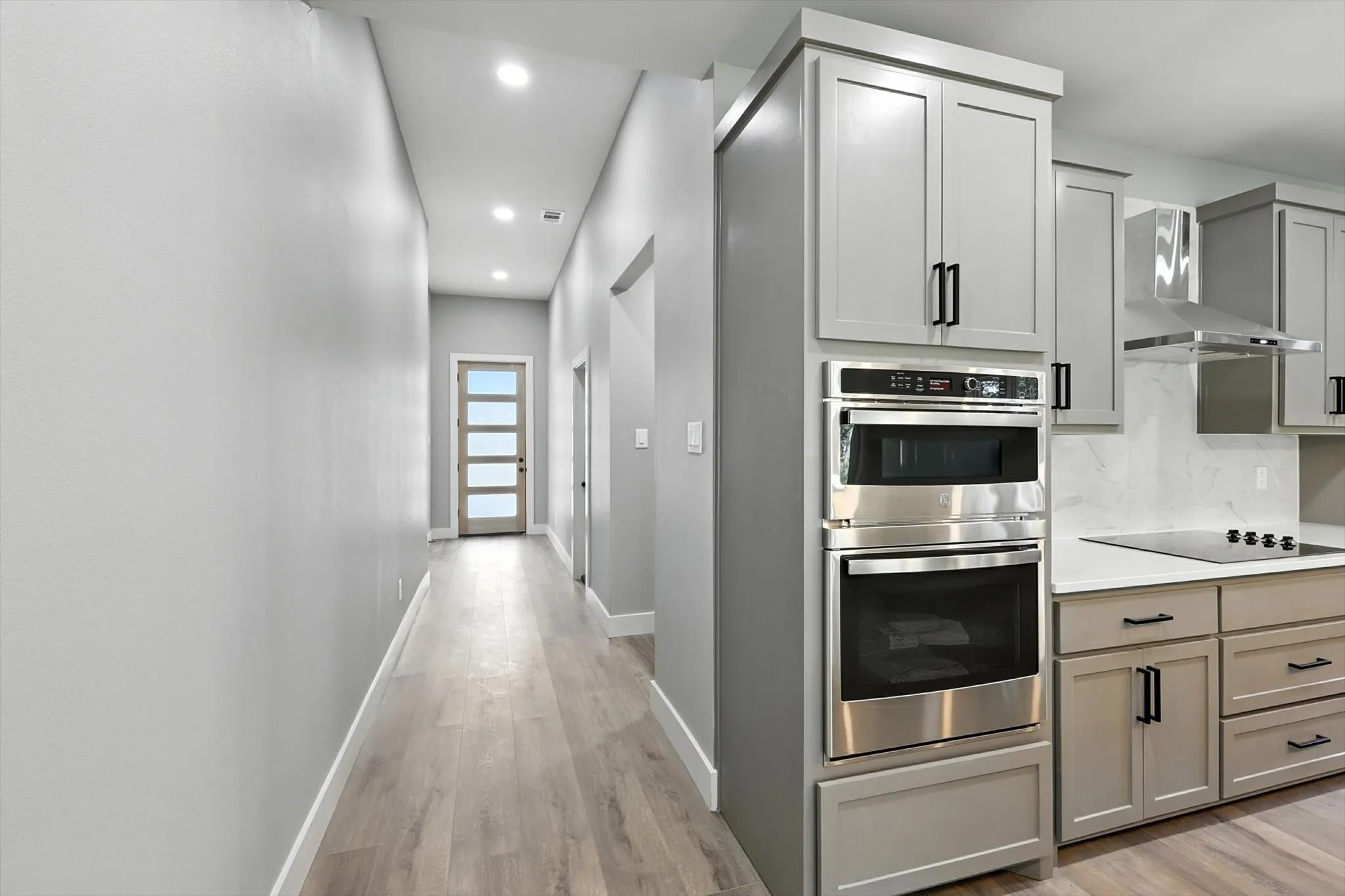 Kitchen with wall chimney range hood, stainless steel double oven, gray cabinets, light wood-style flooring, and recessed lighting