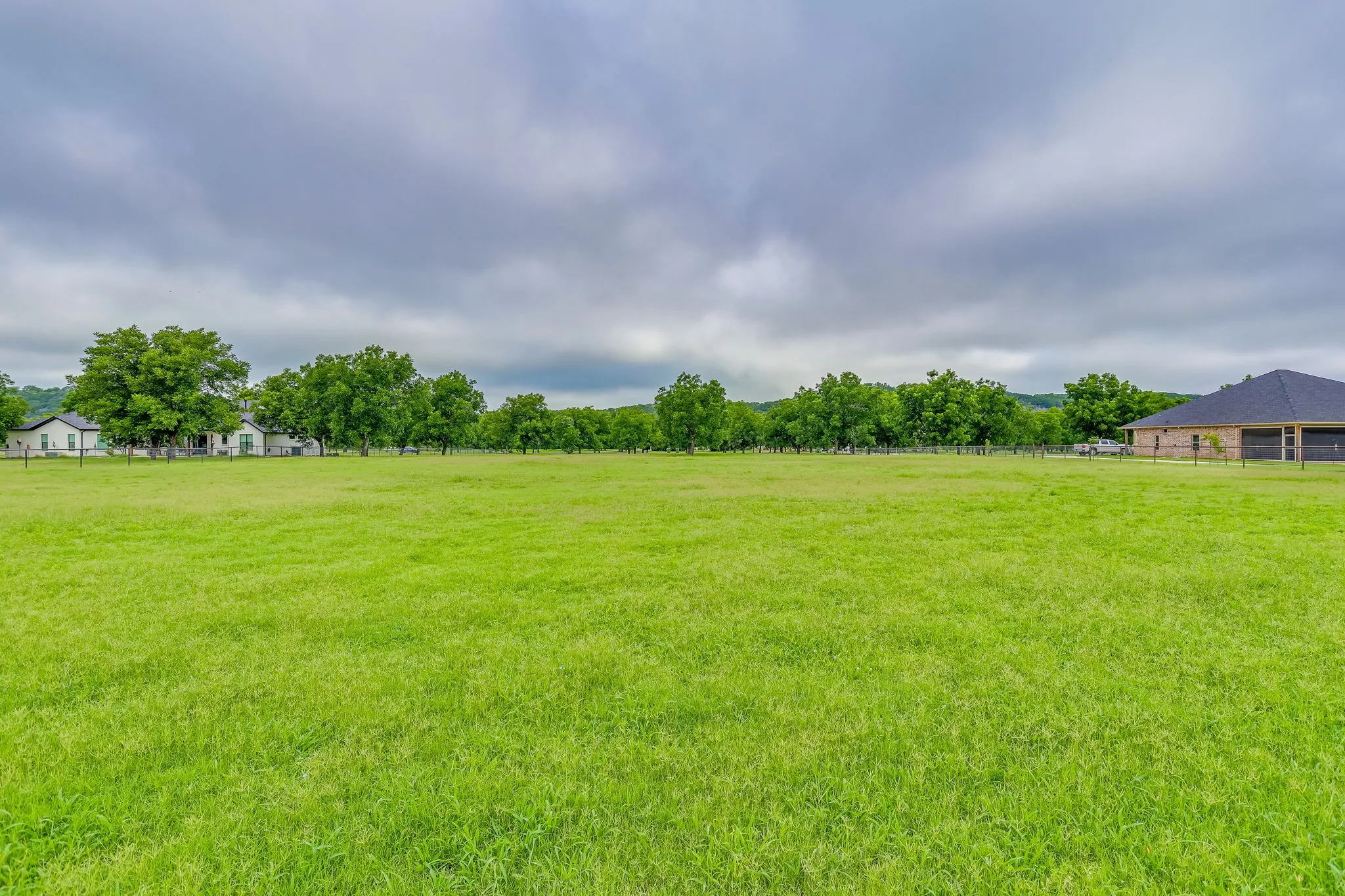 Expansive green land area featuring mature trees and distant residential structures