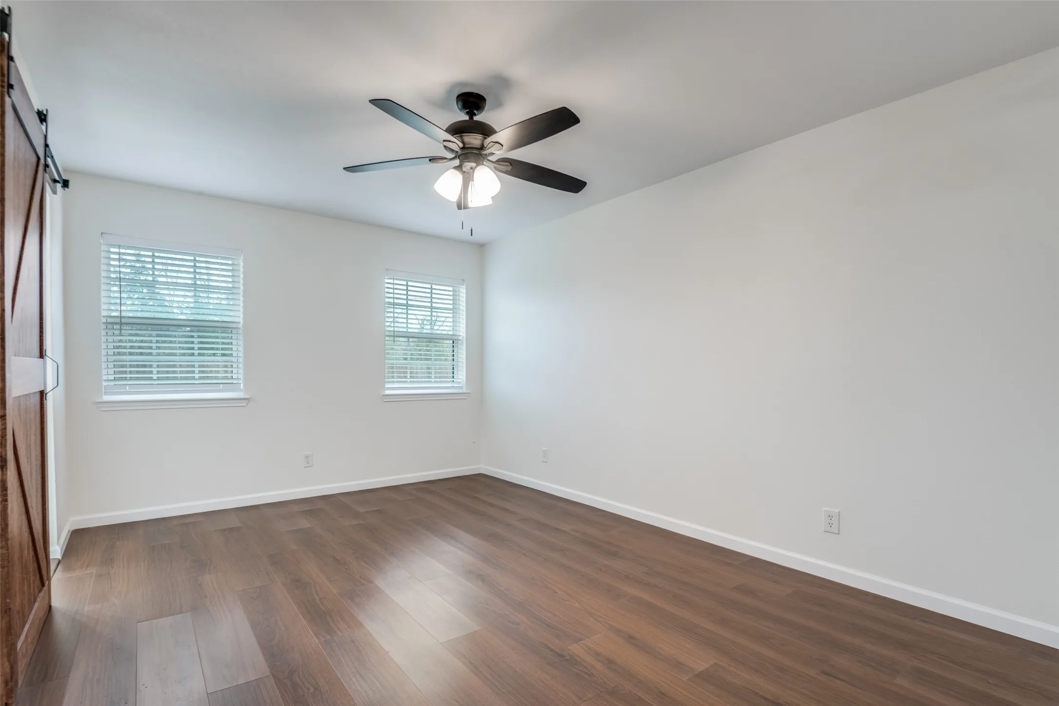 Unfurnished bedroom with a barn door, dark wood-type flooring, and ceiling fan