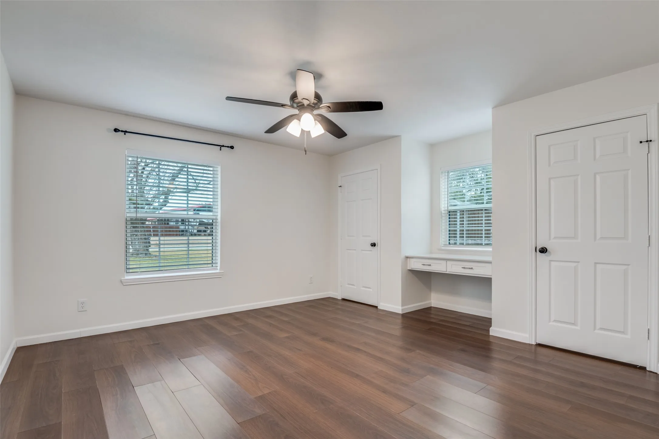 Unfurnished bedroom featuring built in desk, multiple closets, dark wood finished floors, and ceiling fan