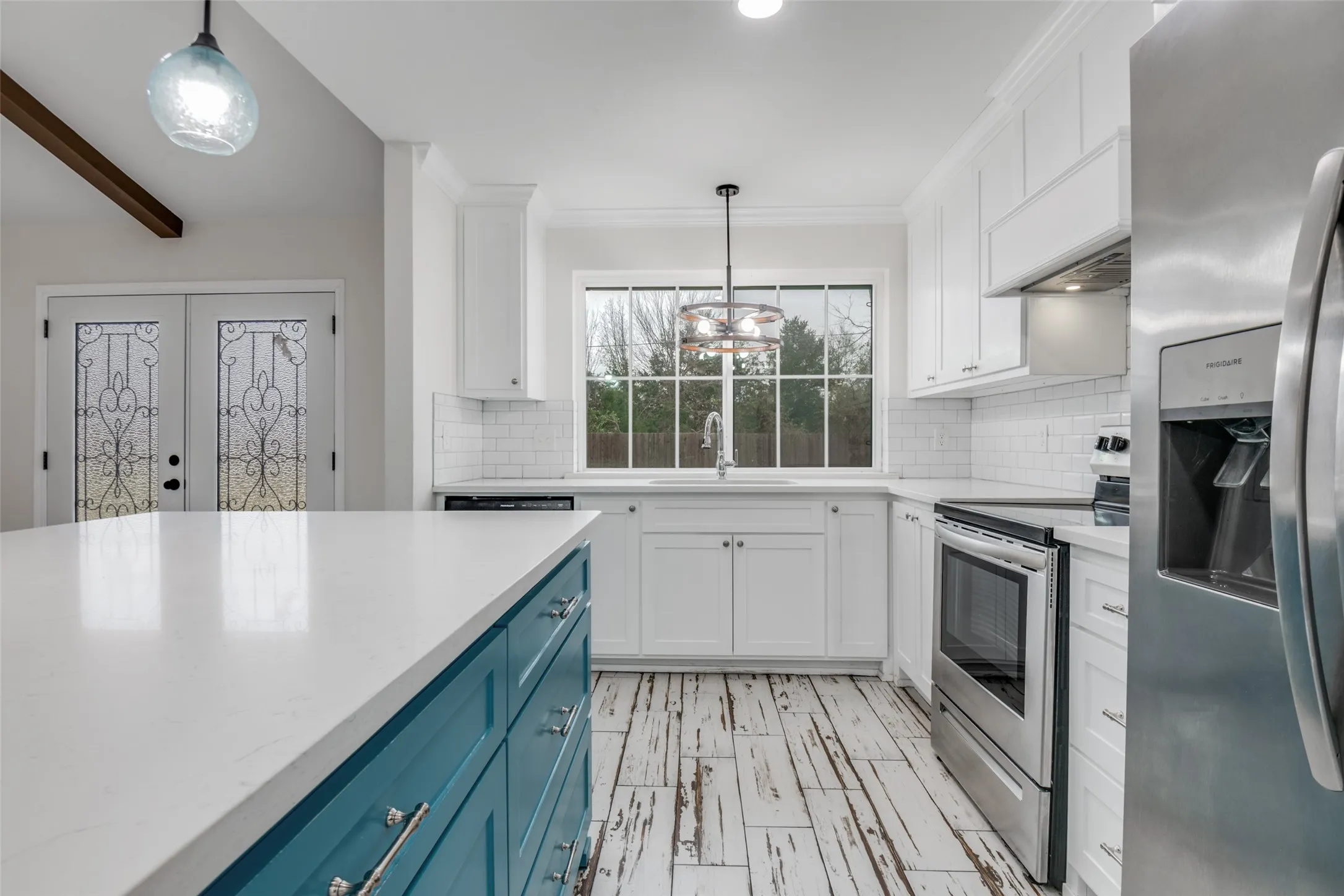 Kitchen featuring appliances with stainless steel finishes, pendant lighting, blue cabinets, white cabinetry, and custom range hood