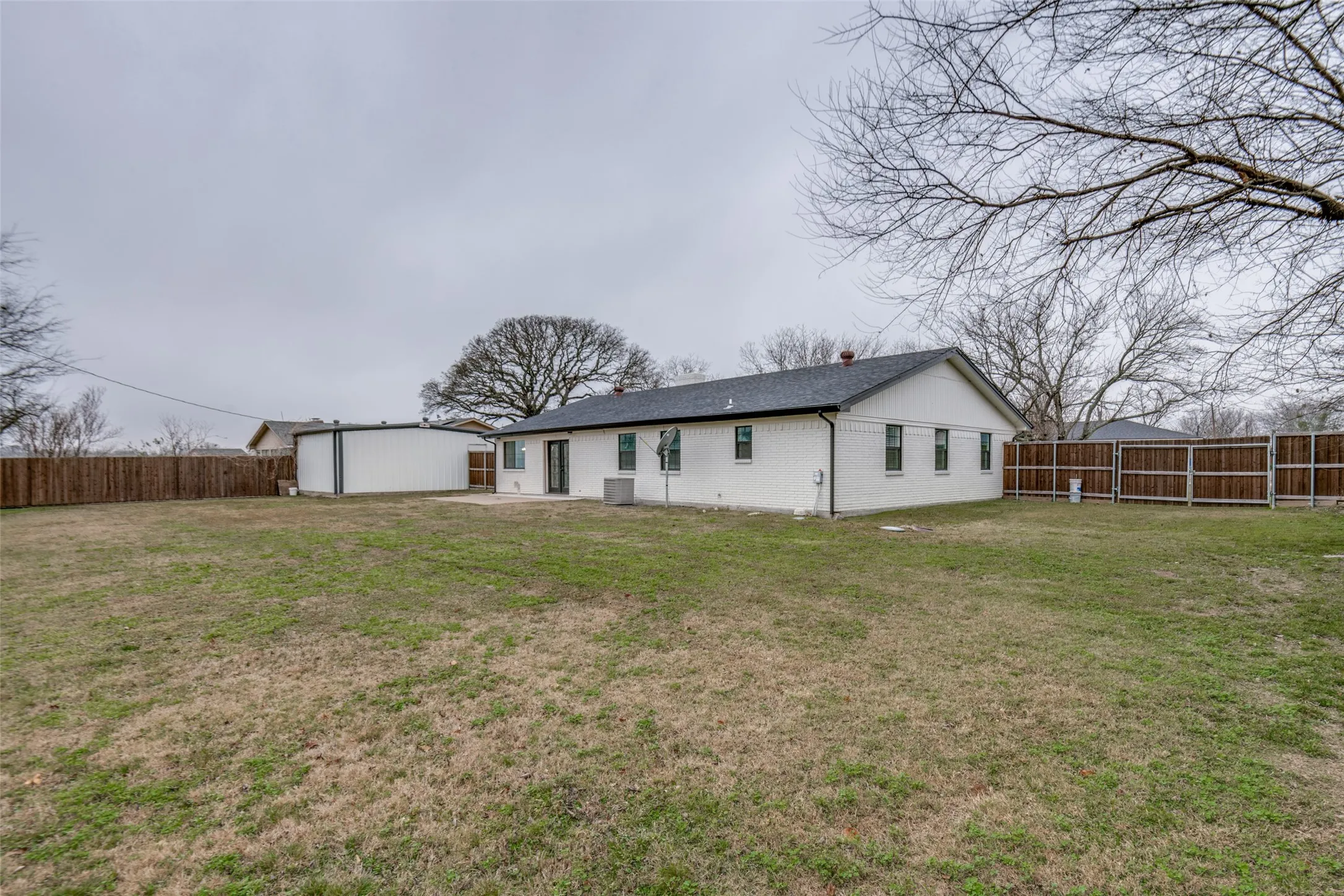 Rear view of house with a fenced backyard, a patio area, brick siding, and an outbuilding