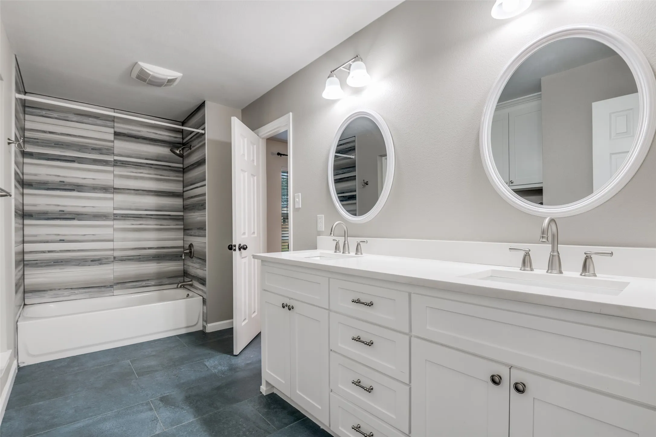 Full bath with shower / bathtub combination, double vanity, and dark tile patterned floors