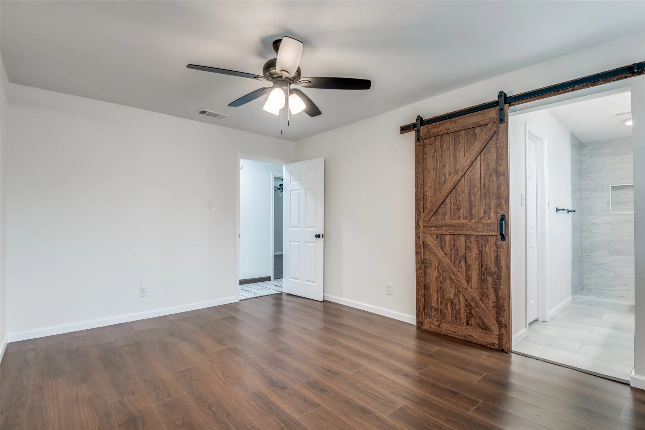 Unfurnished bedroom with a ceiling fan, dark wood-style floors, a barn door, and ensuite bathroom