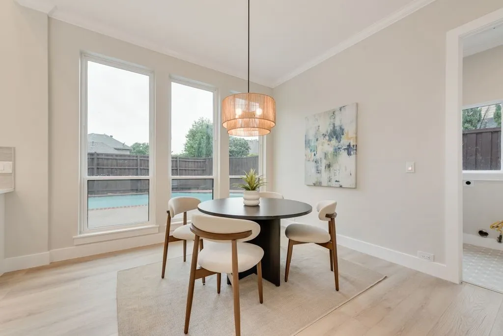 This inviting dining area features light-toned flooring, a modern chandelier, and large windows that overlook a fenced yard with a pool