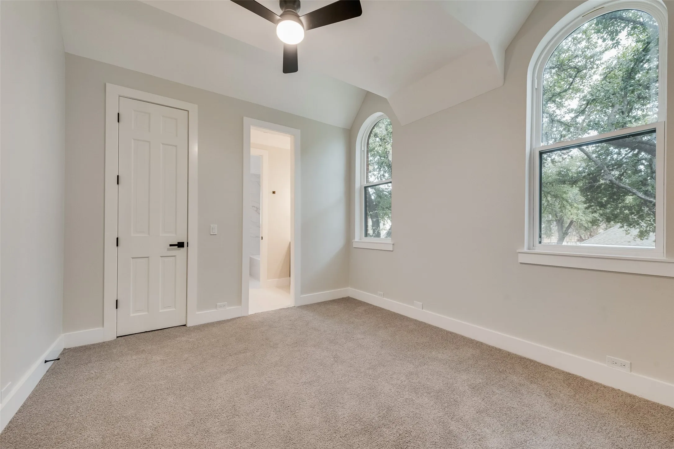 Unfurnished bedroom featuring vaulted ceiling, light carpet, connected bathroom, and a ceiling fan