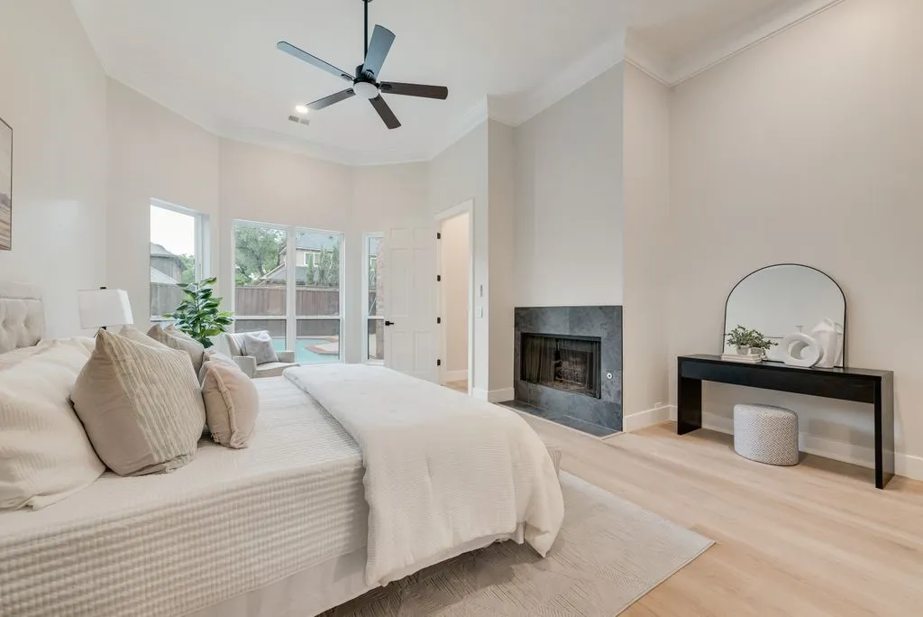 This room offers high ceilings with crown molding, light-toned flooring, and a fireplace with a dark stone surround