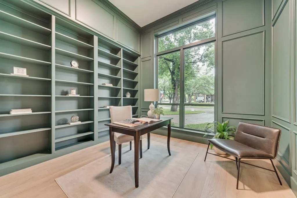 The room features extensive built-in shelving, panel molding on the walls, and a large window providing ample natural light and views of the exterior