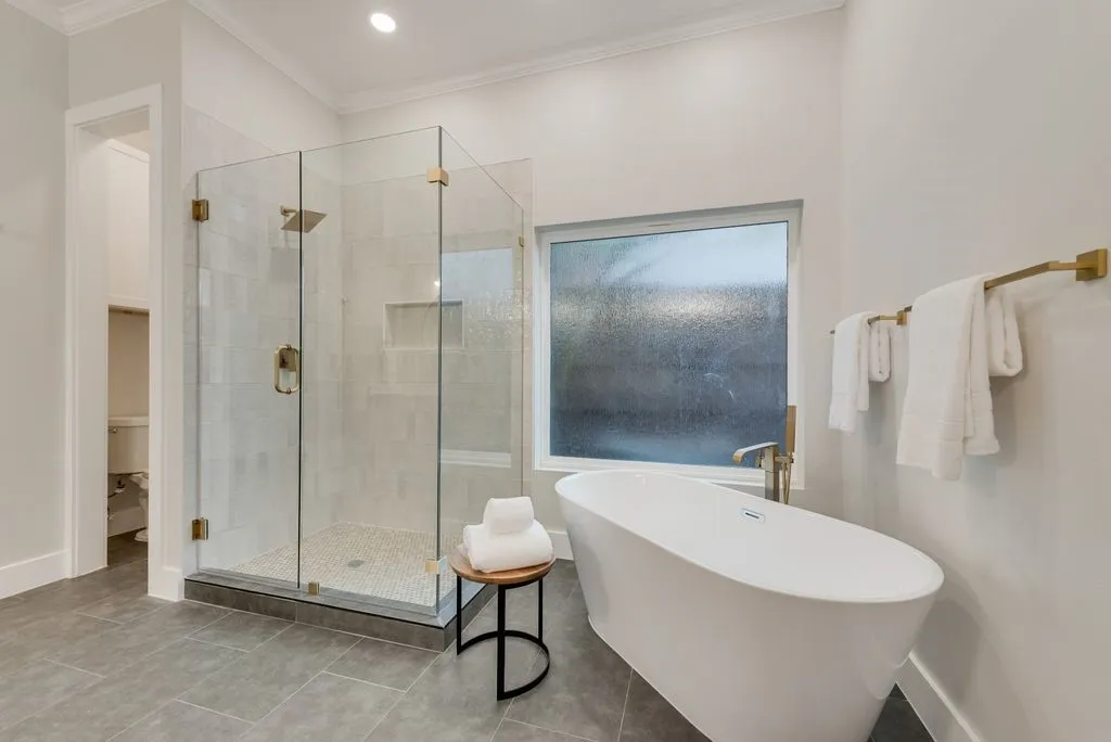 Bathroom featuring a glass-enclosed shower with gold-toned fixtures, a freestanding soaking tub, and a window providing natural light