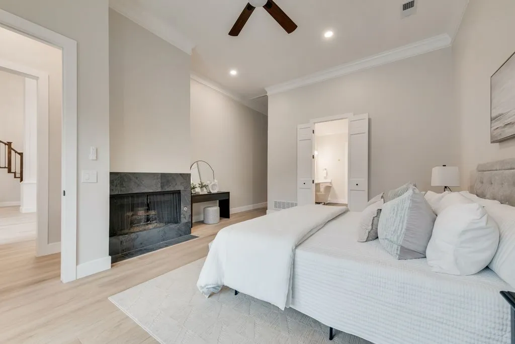 This inviting interior features light-toned flooring, a fireplace with a dark stone surround, and crown molding