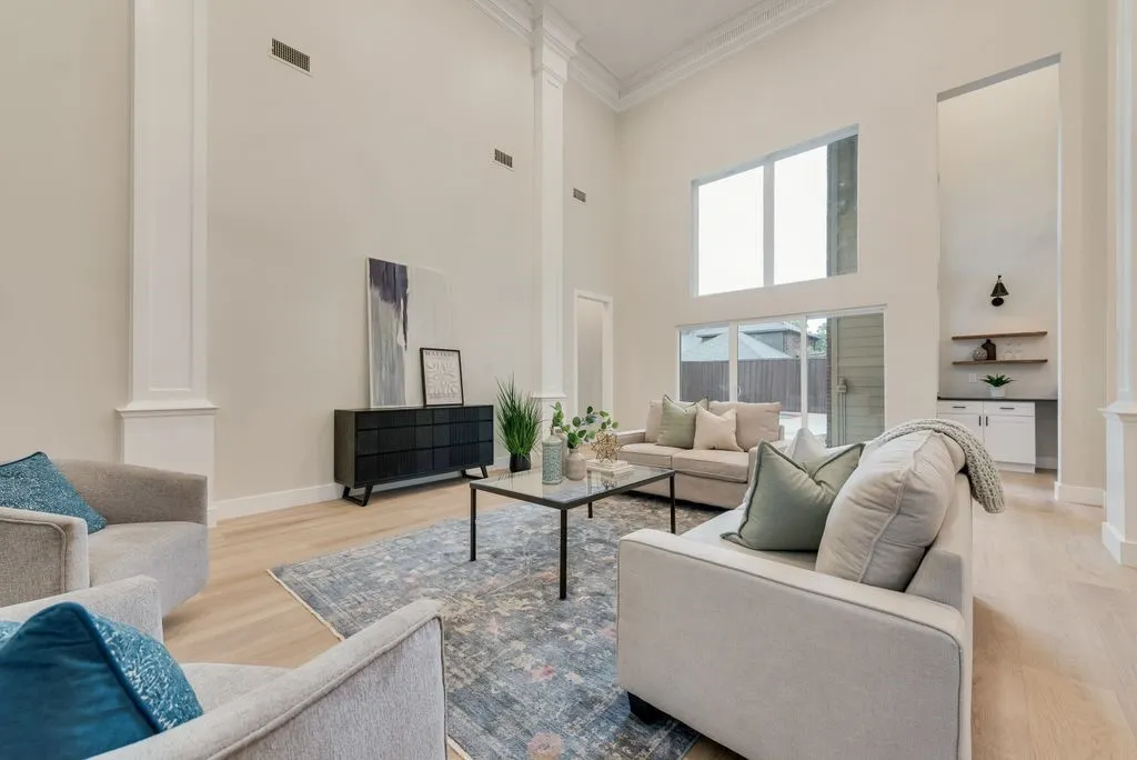 This spacious living area features high ceilings with crown molding, light wood flooring, and large windows providing natural light