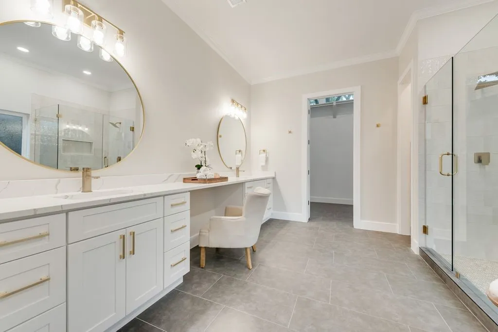 This bathroom features a double vanity with white cabinetry, gold hardware, and quartz countertops