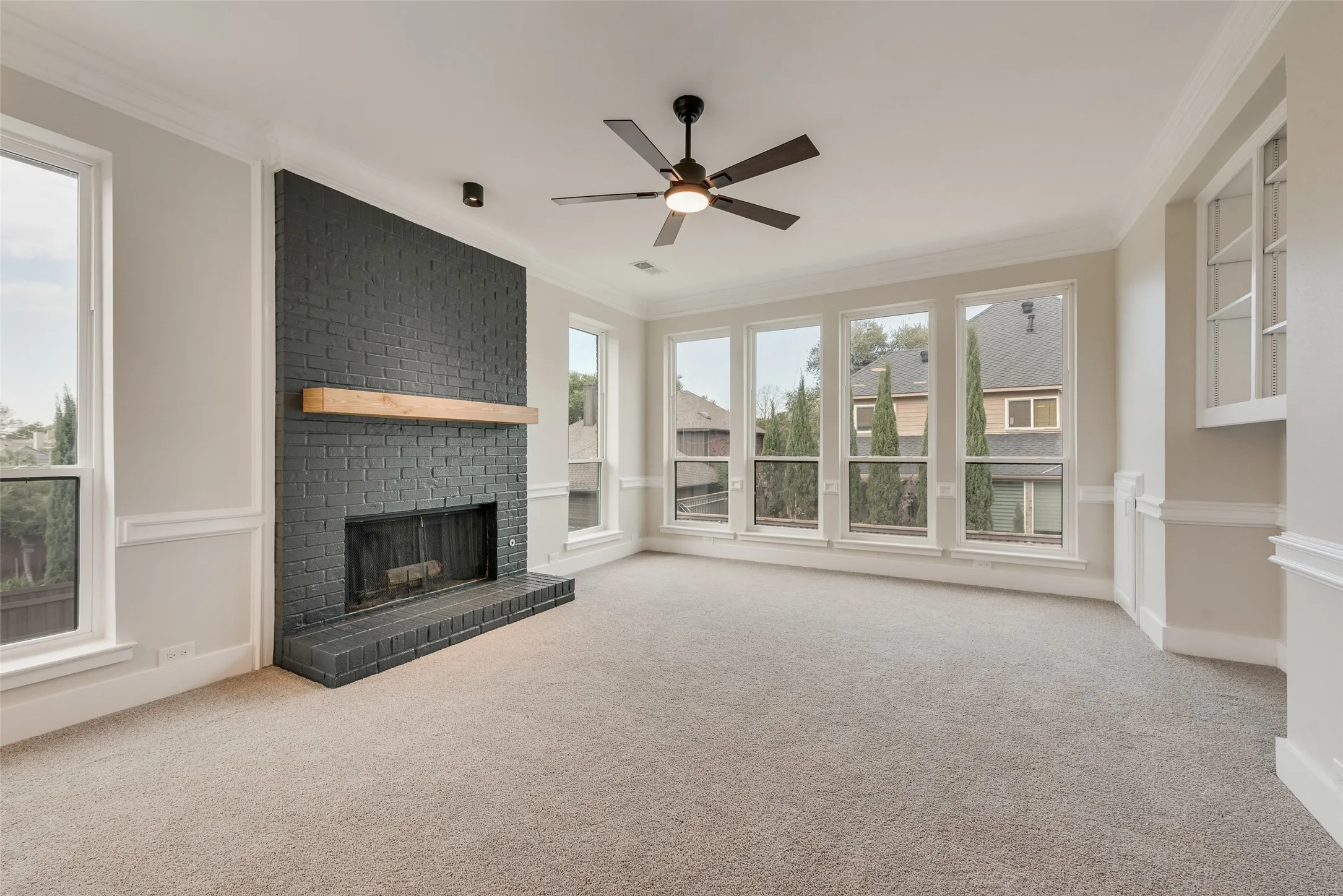 Unfurnished living room featuring crown molding, light carpet, a fireplace, and a ceiling fan