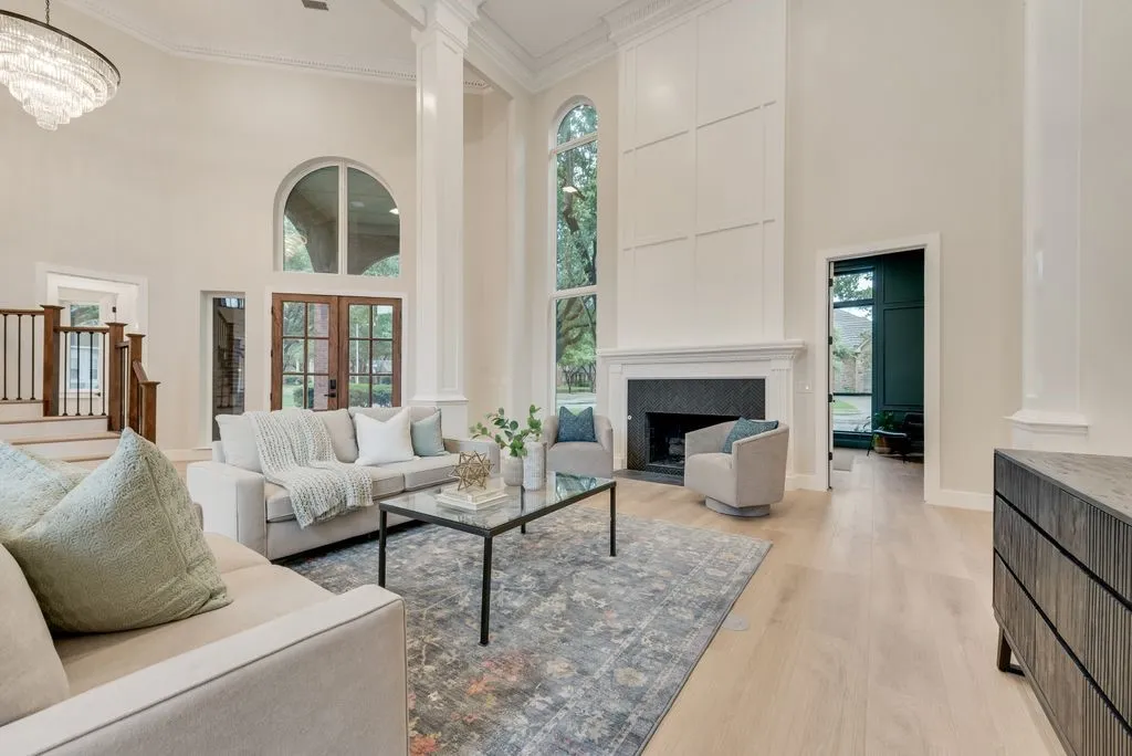 The living area features a high ceiling, hardwood floors, and a fireplace with a black surround and white mantel