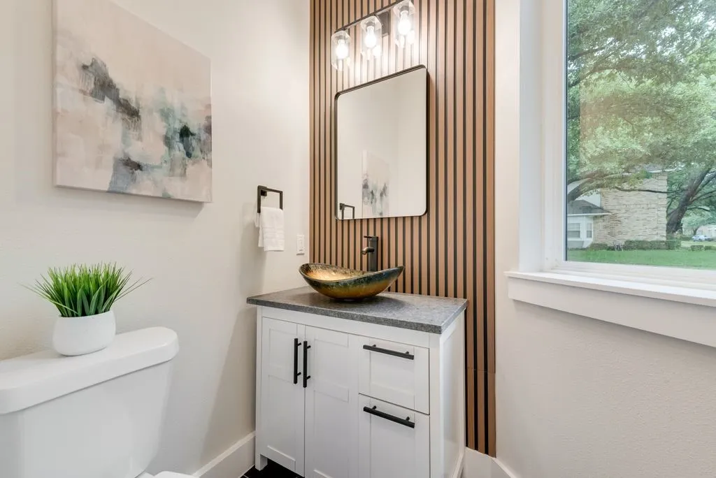Bathroom featuring a white vanity with dark hardware, a vessel sink, and a modern slatted accent wall