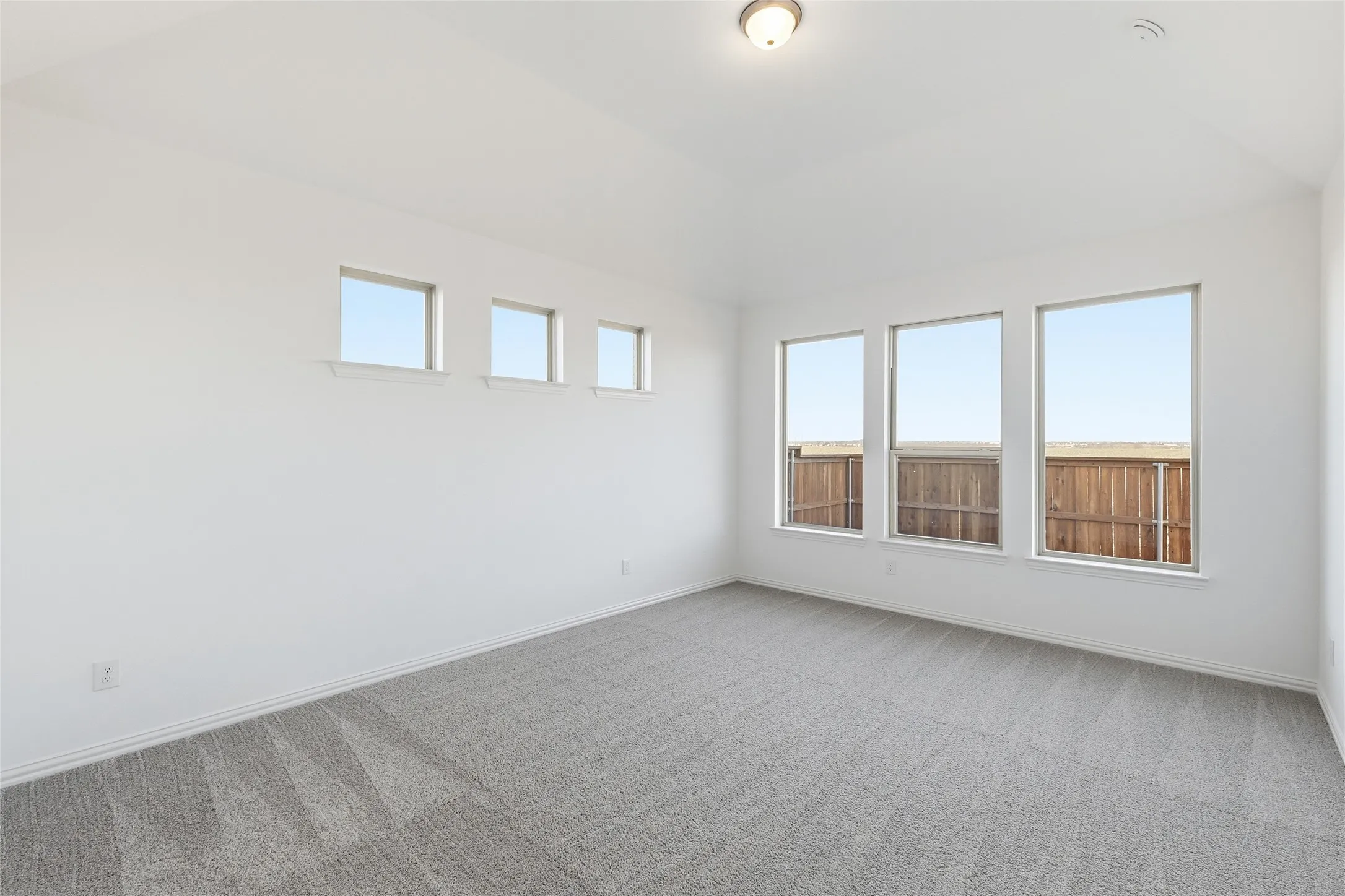 Spacious room featuring vaulted ceilings, a contemporary flush-mount light fixture, and plush gray carpeting