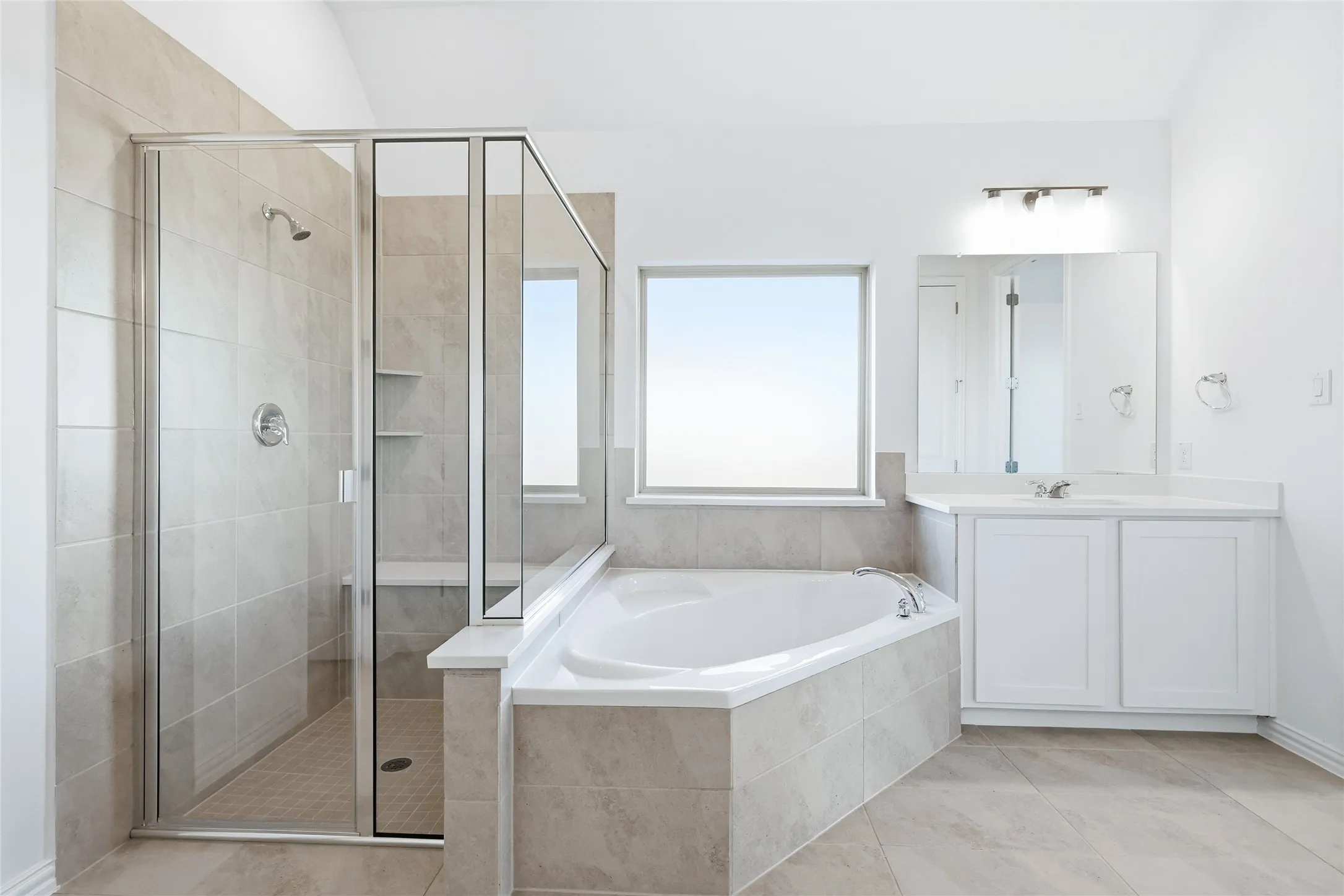 Bathroom featuring a corner soaking tub, a separate glass-enclosed shower with tiled walls and a built-in bench, a single vanity with white cabinetry, and a rectangular window