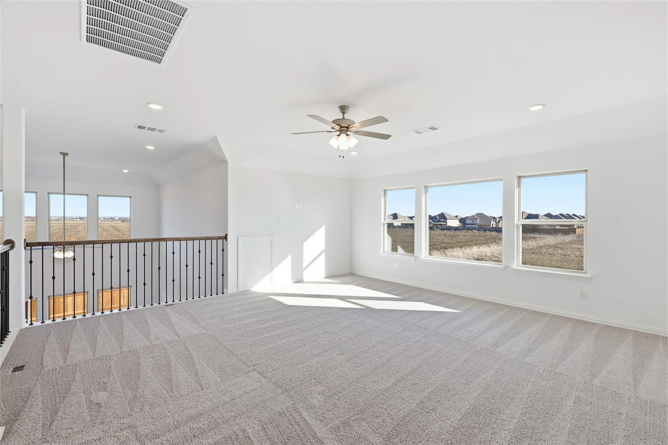 Spacious upstairs loft featuring light-toned carpet, multiple windows, recessed lighting, and a ceiling fan