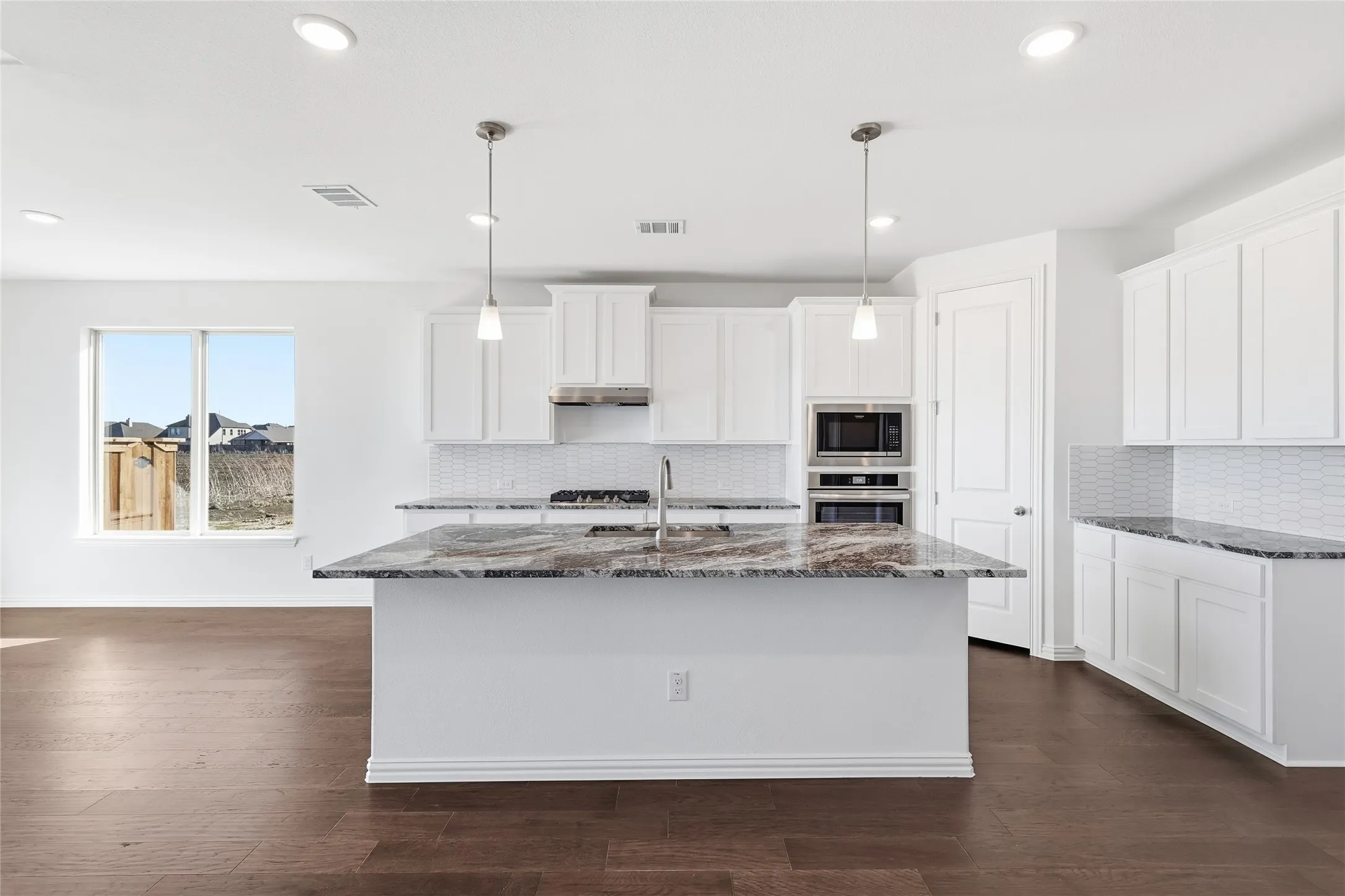 Kitchen featuring a large island with stone countertops, white cabinetry, built-in stainless steel appliances, a white tile backsplash, and wood-finish flooring