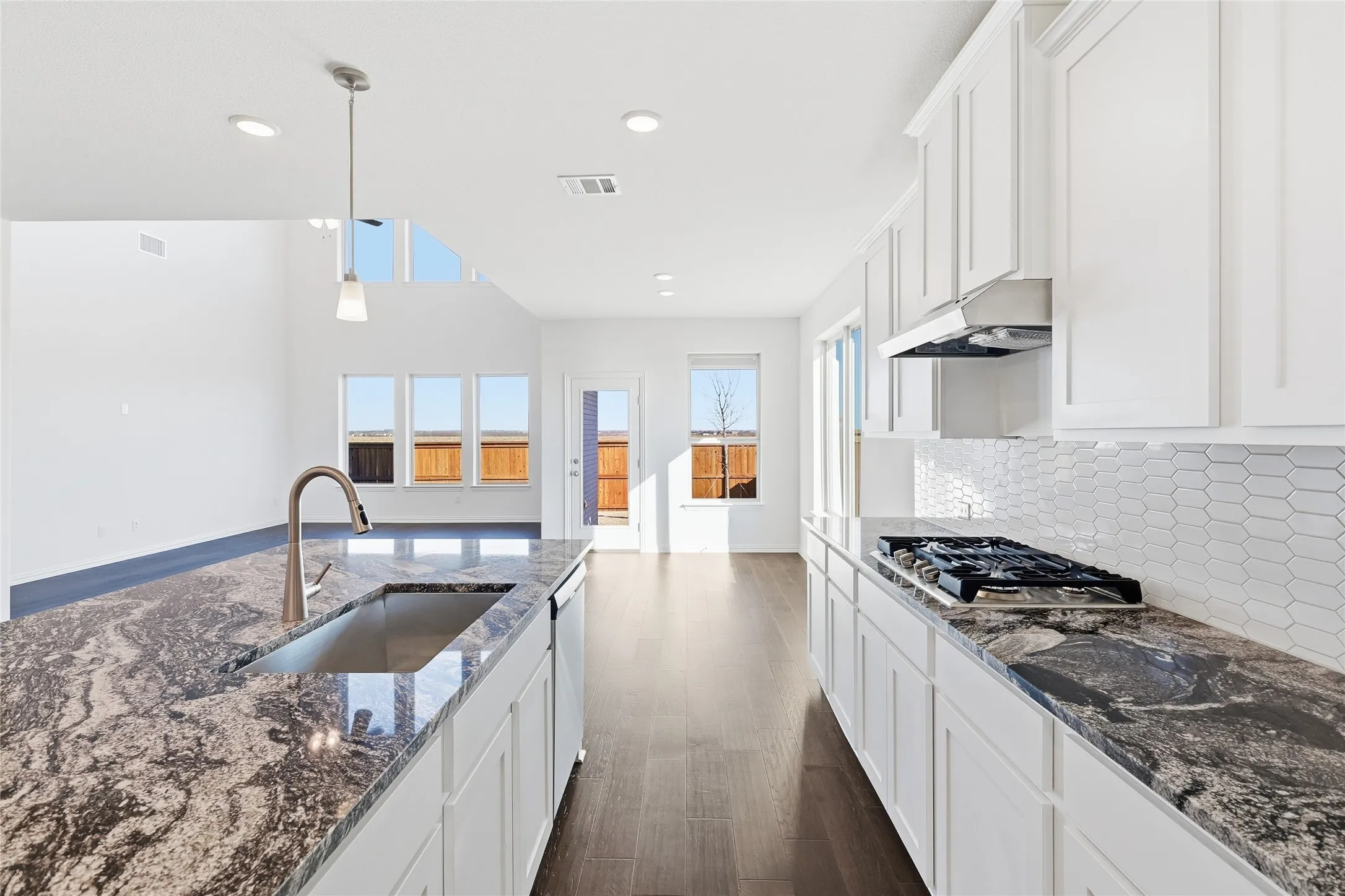 Kitchen featuring white cabinetry, dark patterned countertops, a stainless steel undermount sink with a gooseneck faucet, a built-in gas cooktop, and a geometric tile backsplash
