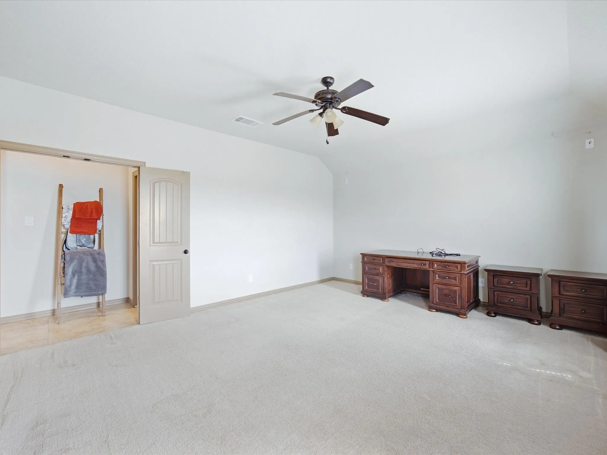 Spacious room featuring vaulted ceilings, light-toned carpeting, a ceiling fan with integrated lighting, and a paneled interior door