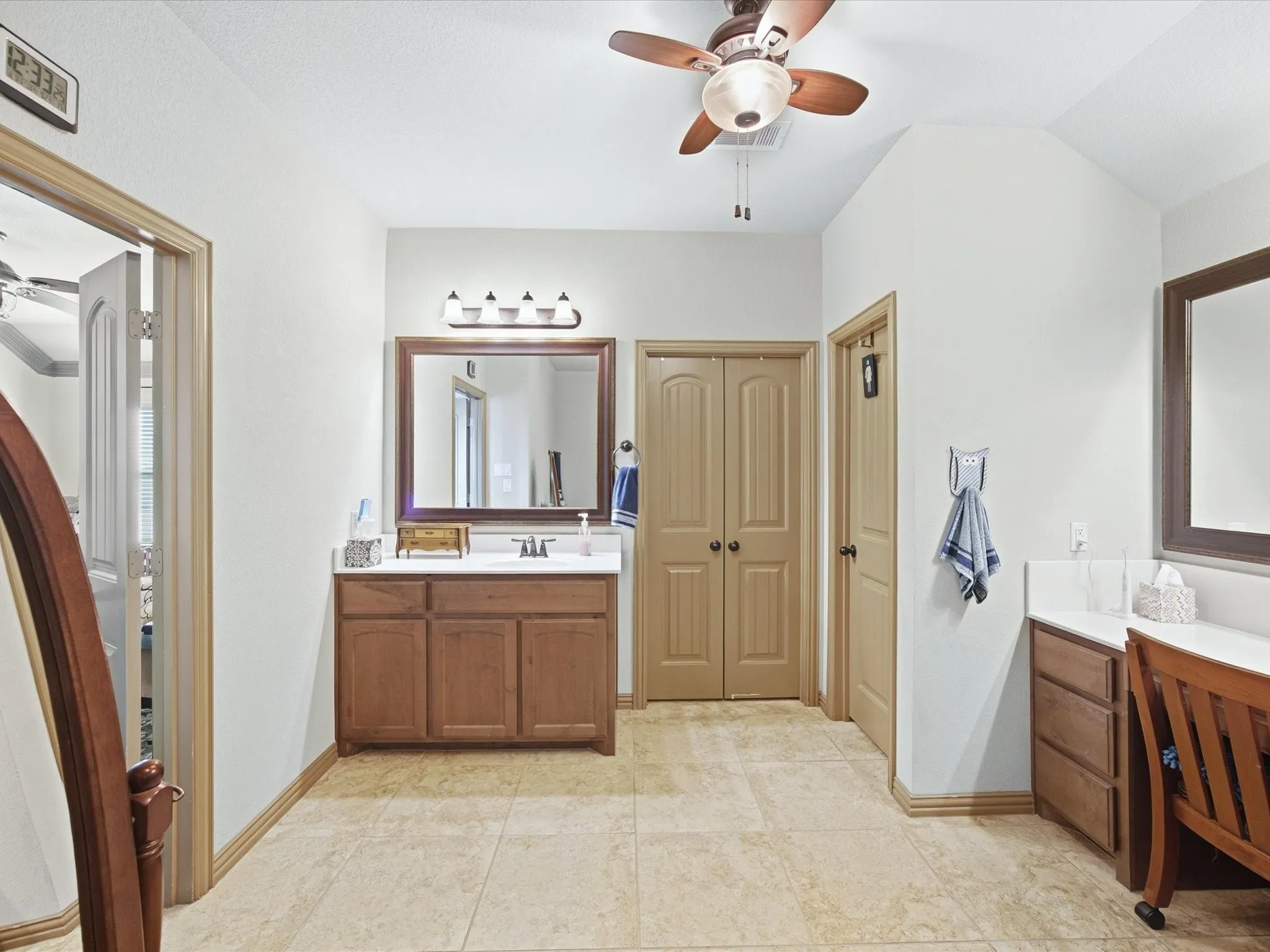 Vaulted ceiling with a ceiling fan, dual vanity spaces with wood cabinetry, and tiled flooring