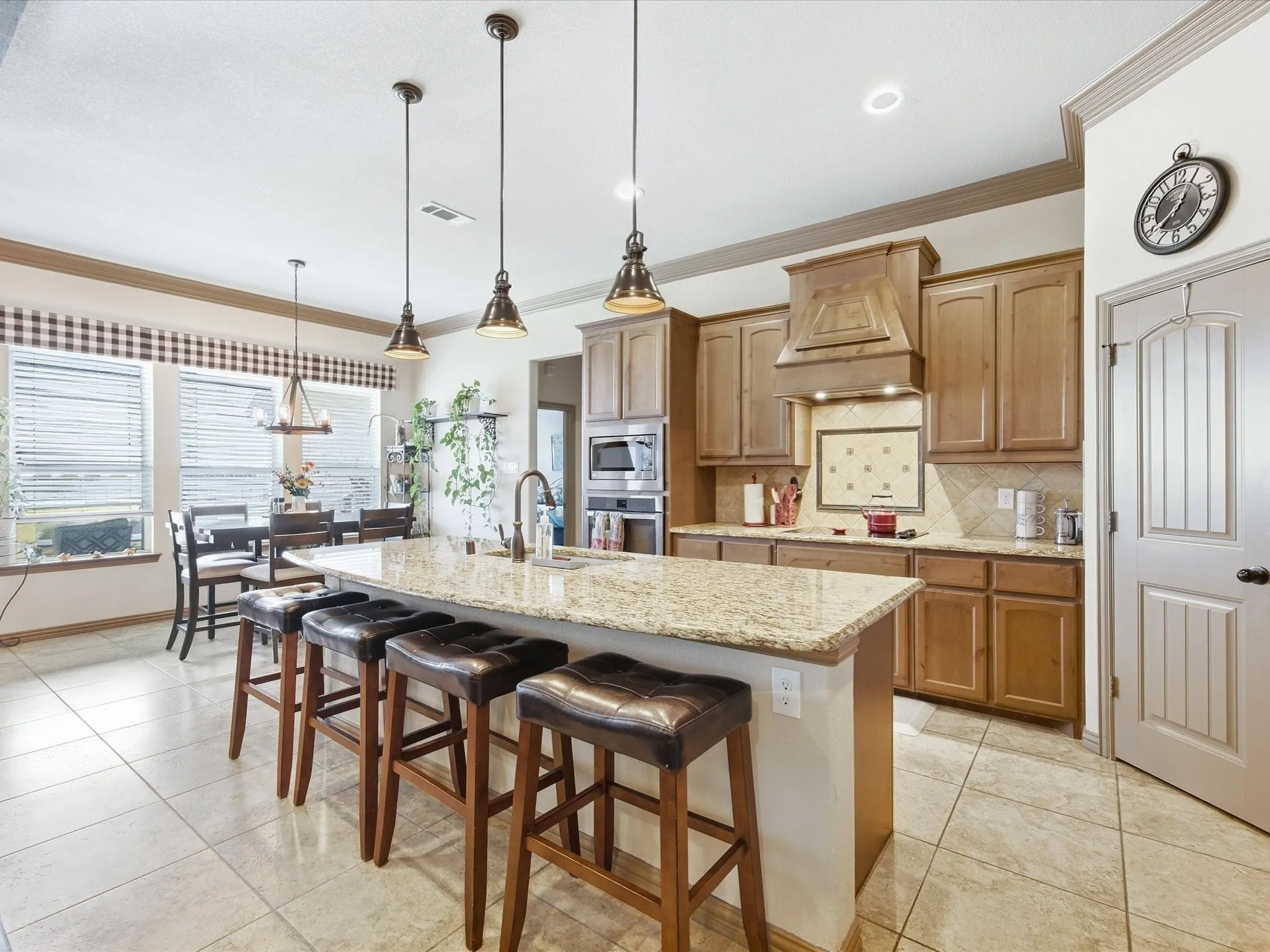 Kitchen featuring a large island with stone countertop, wood cabinetry, tile flooring, built-in appliances, and pendant lighting