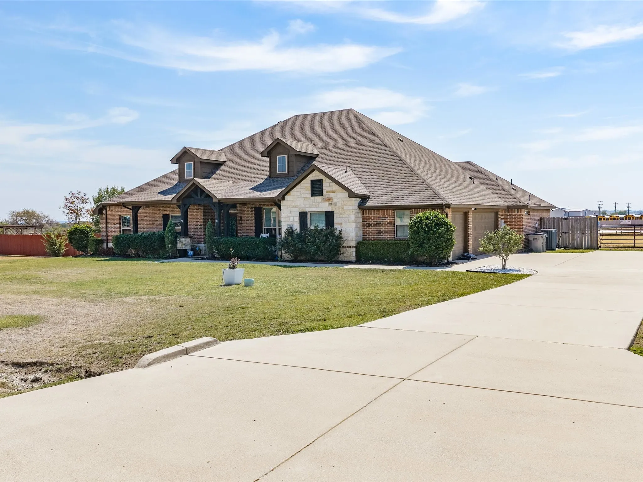 Brick and stone exterior with dark shutters, gabled dormers, a covered entry, and a multi-car concrete driveway