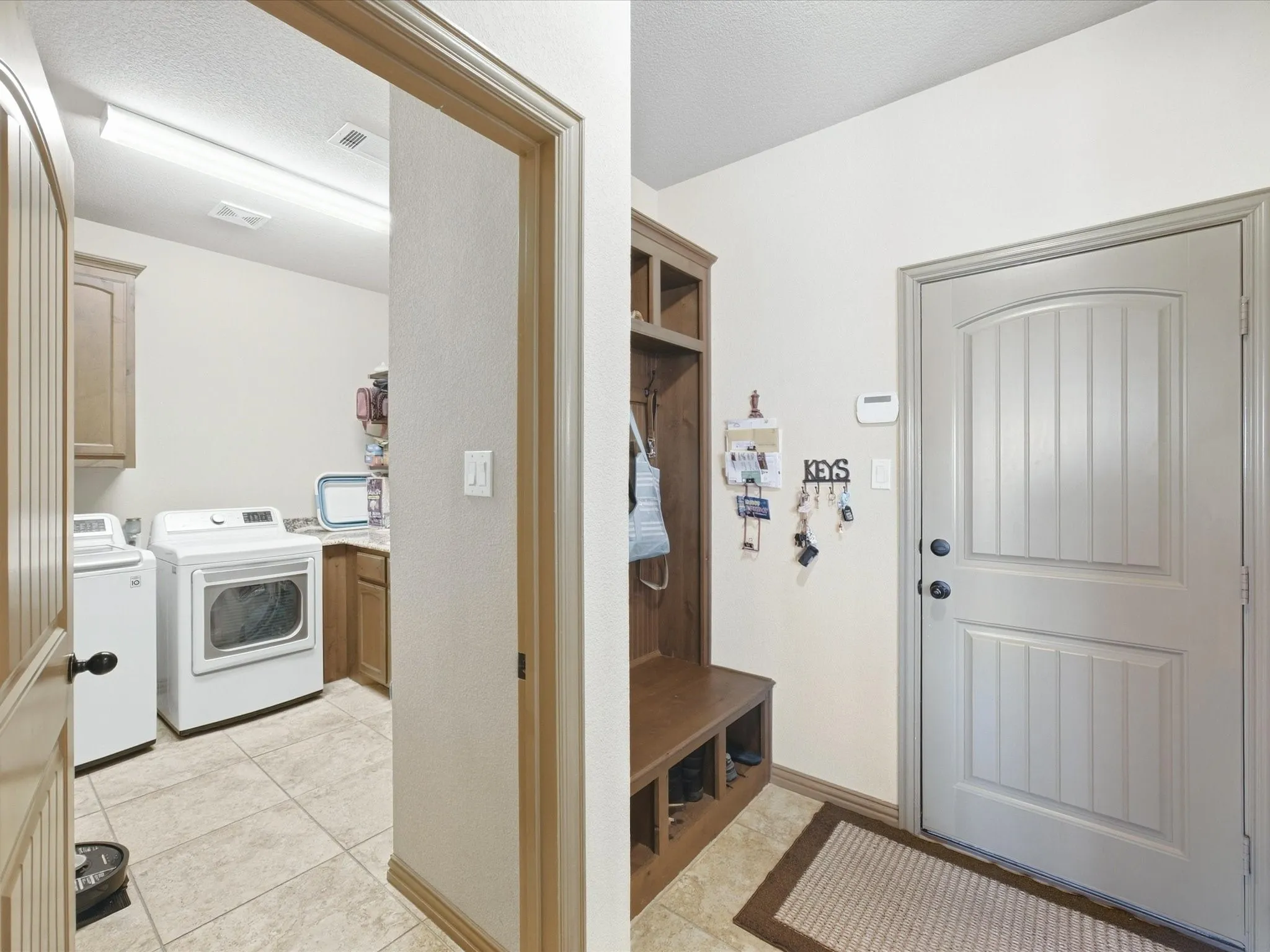 Integrated wood-finish built-in storage bench, paneled entry door, laundry room with tiled flooring, and wood-finish cabinetry