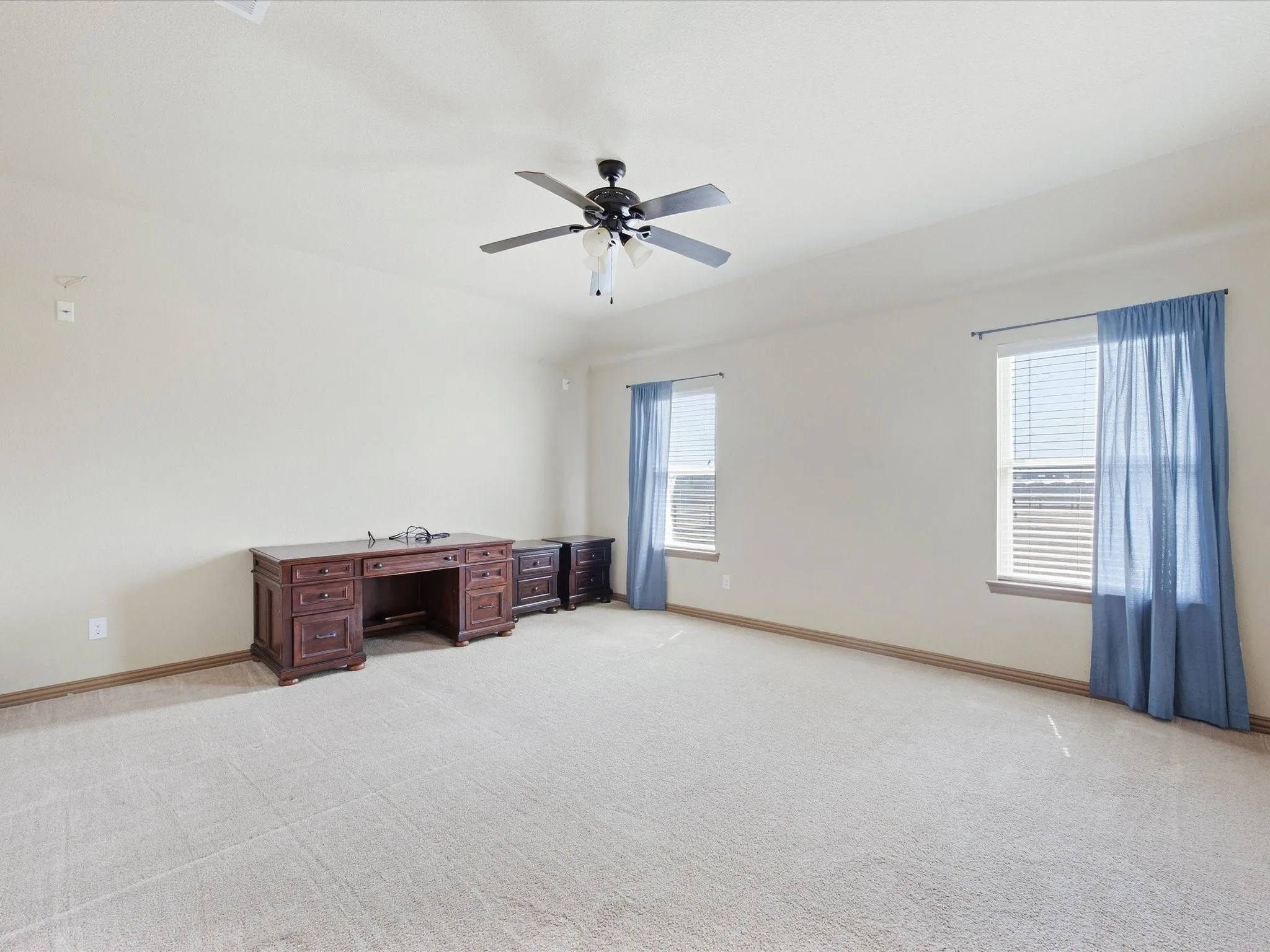 Spacious room with light-colored carpeting, two windows, and a ceiling fan