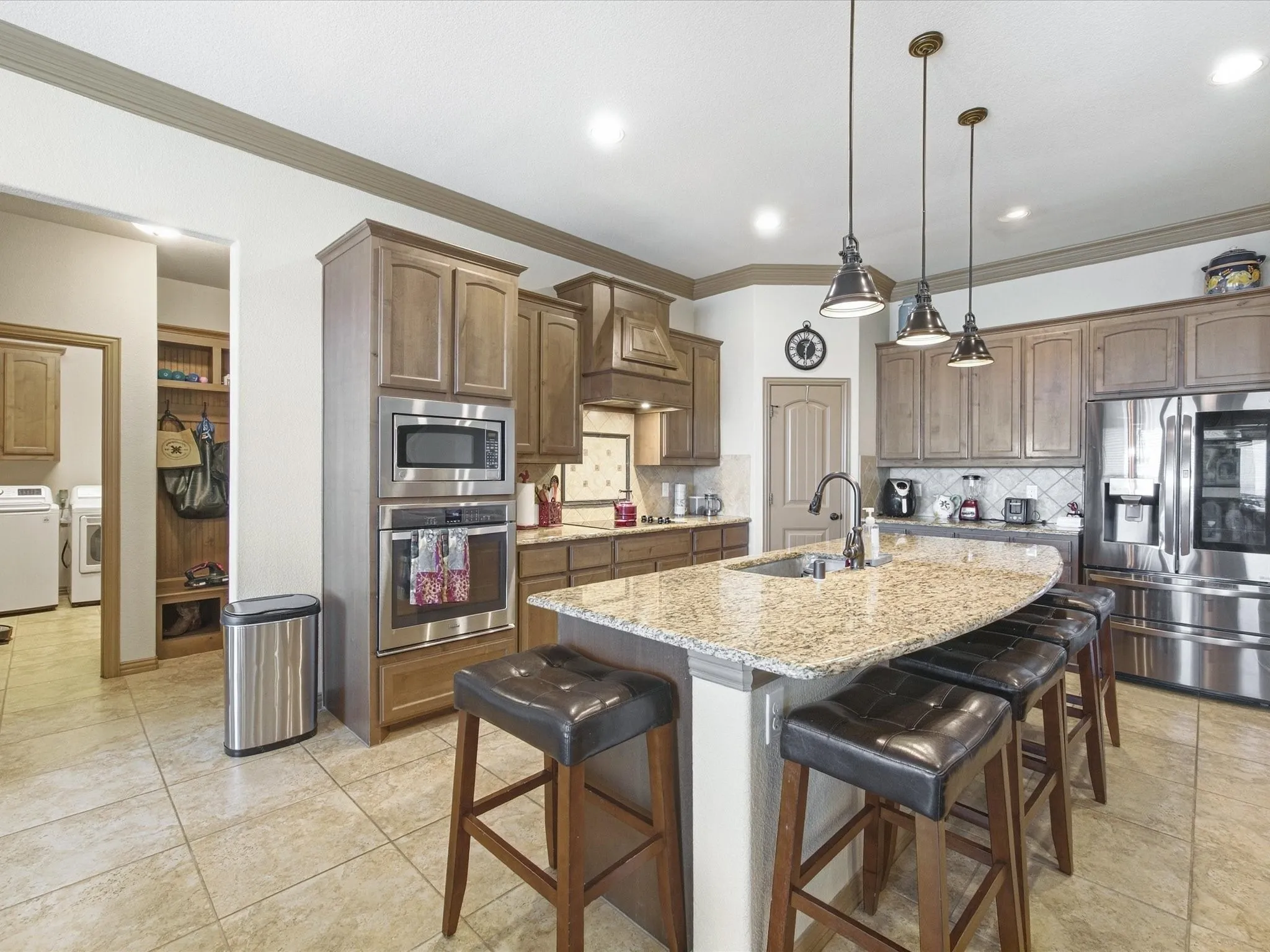 Spacious kitchen featuring an expansive island with an undermount sink, pendant lighting, built-in stainless steel appliances, and wood-finish cabinetry