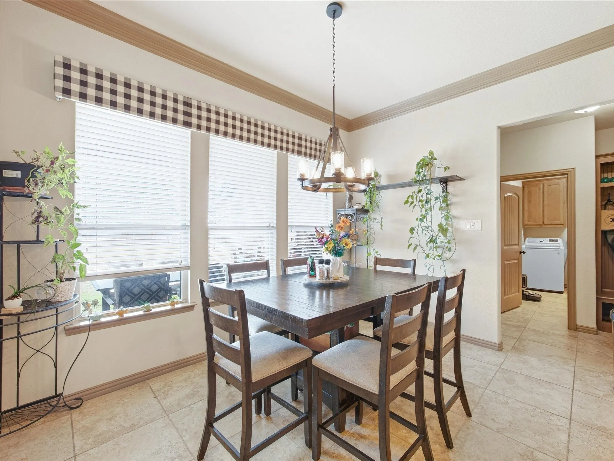 Tile flooring throughout, natural light from multiple windows, crown molding, and a visible utility space with built-in cabinetry